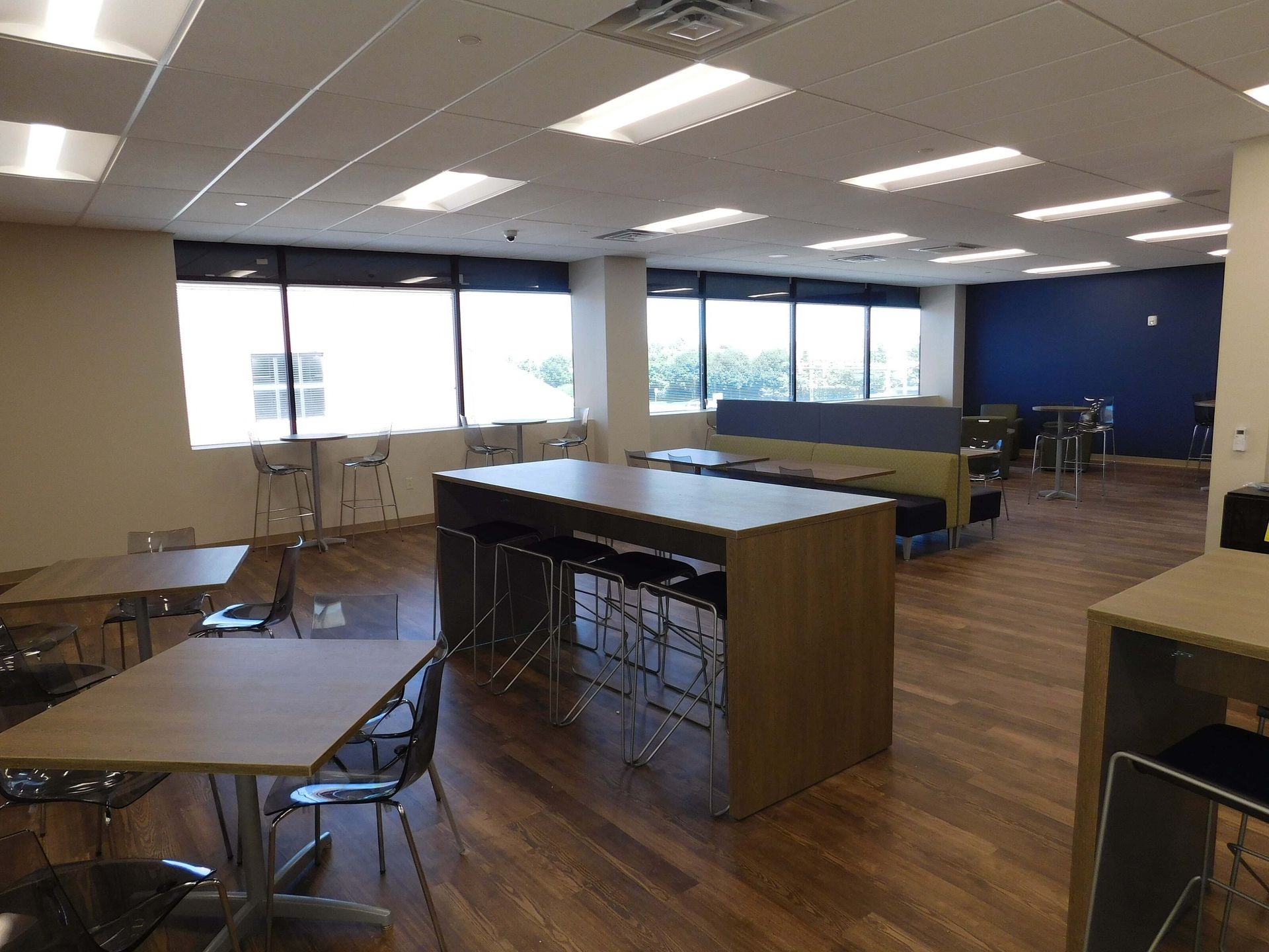 Empty modern classroom with tables, chairs, windows, and a central island counter under fluorescent lights