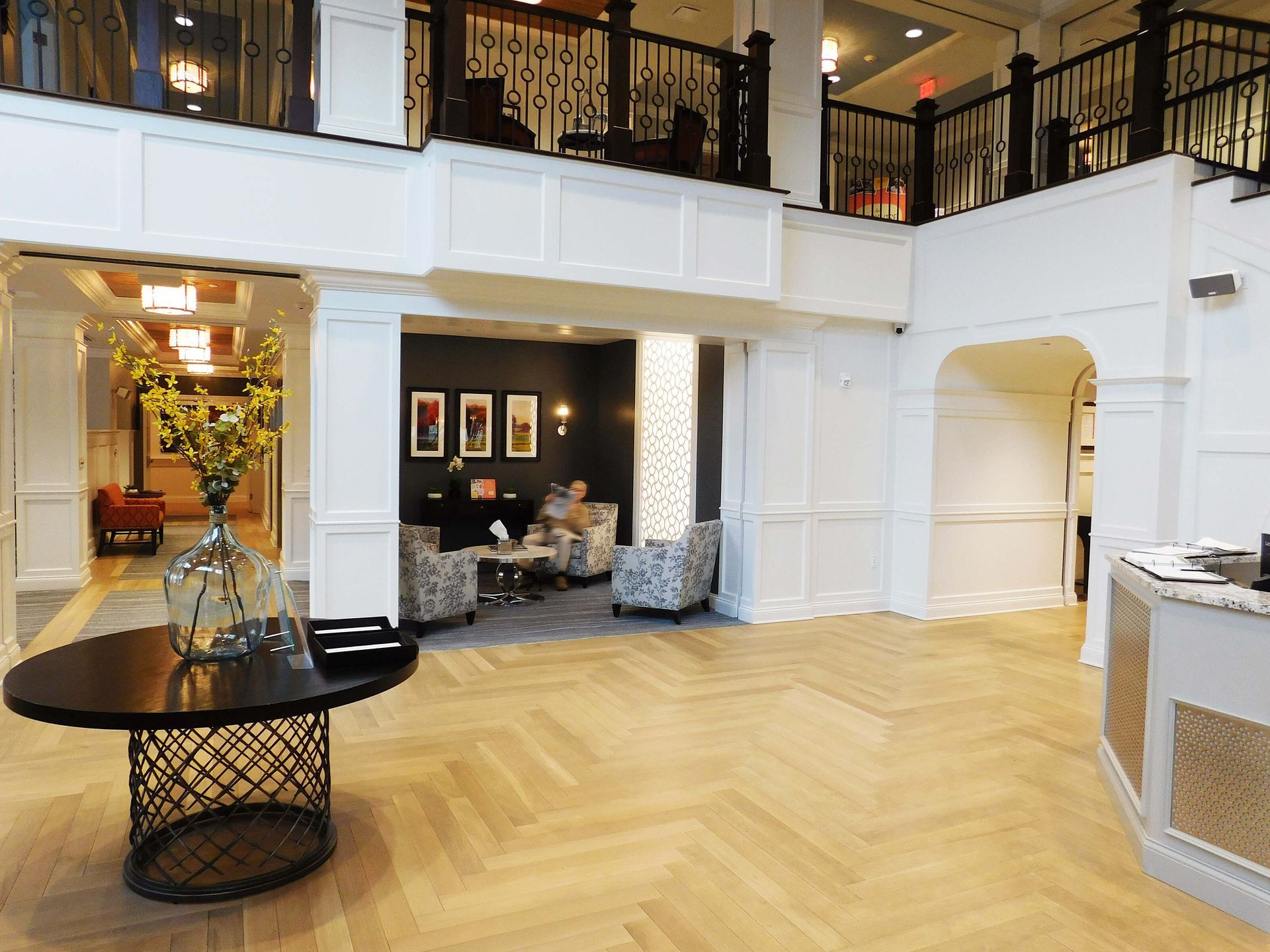 Elegant hotel lobby with white columns, herringbone wood floor, and black balcony railings