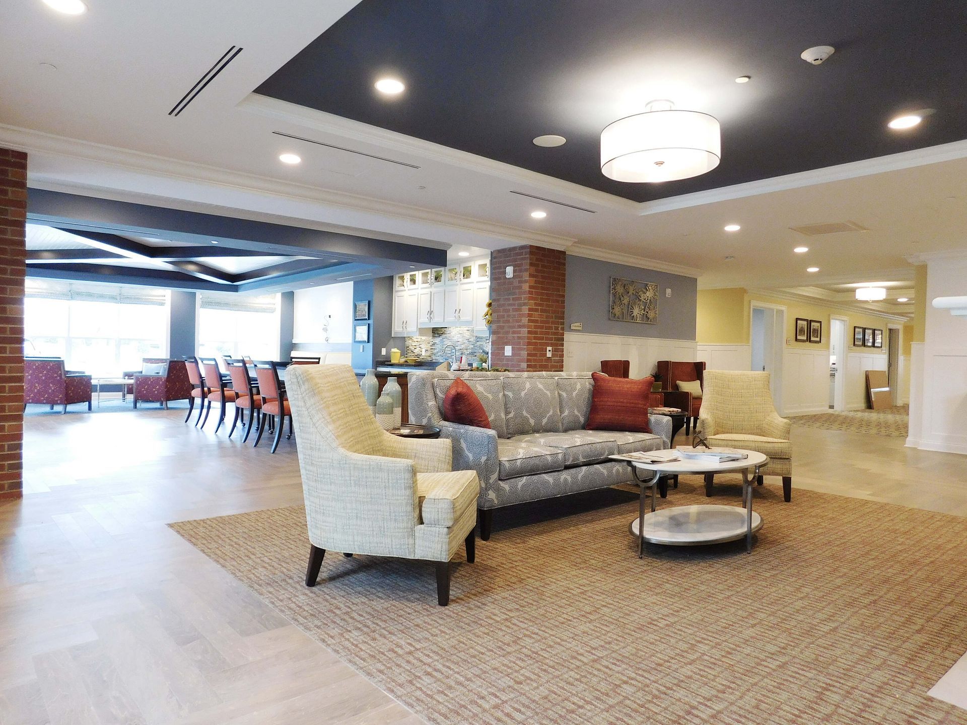 Modern hotel lobby with beige armchairs, red sofas, coffee tables, and dining area in the background