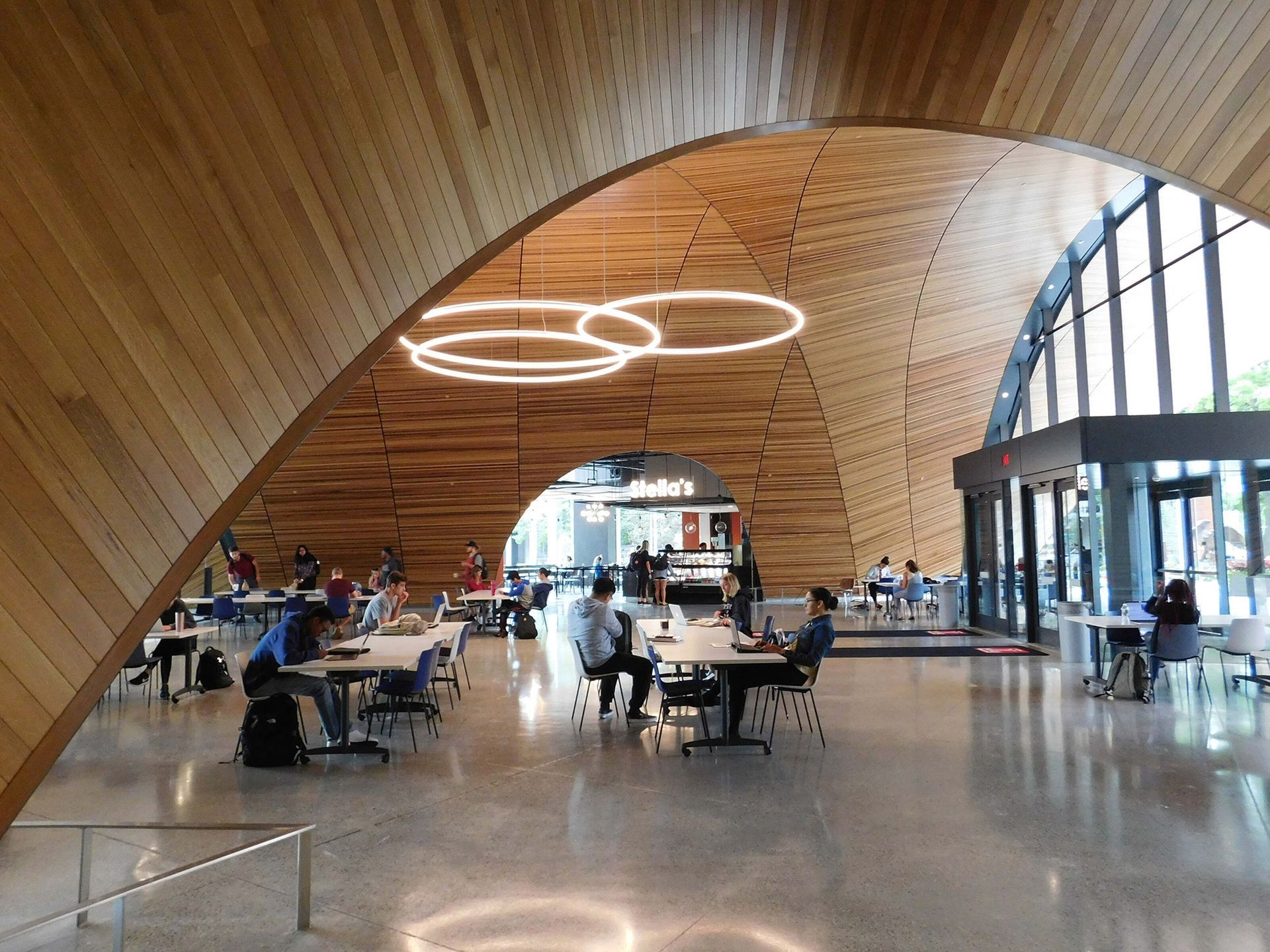 Modern airport terminal with wood ceiling, circular lights, and travelers seated at tables