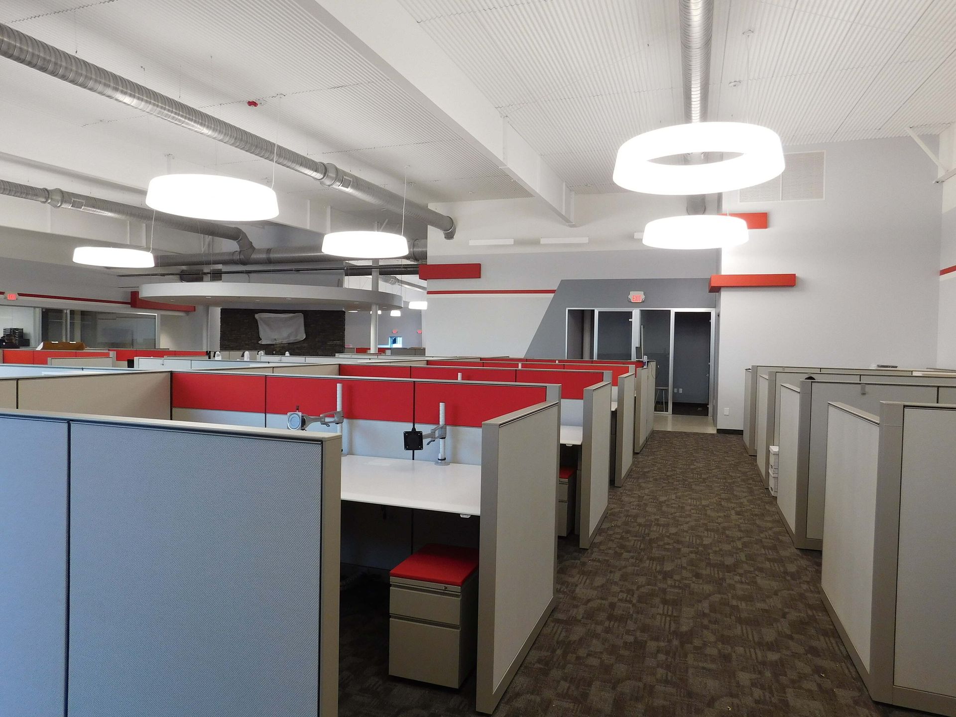 Open office with rows of gray cubicles, red dividers, and circular ceiling lights