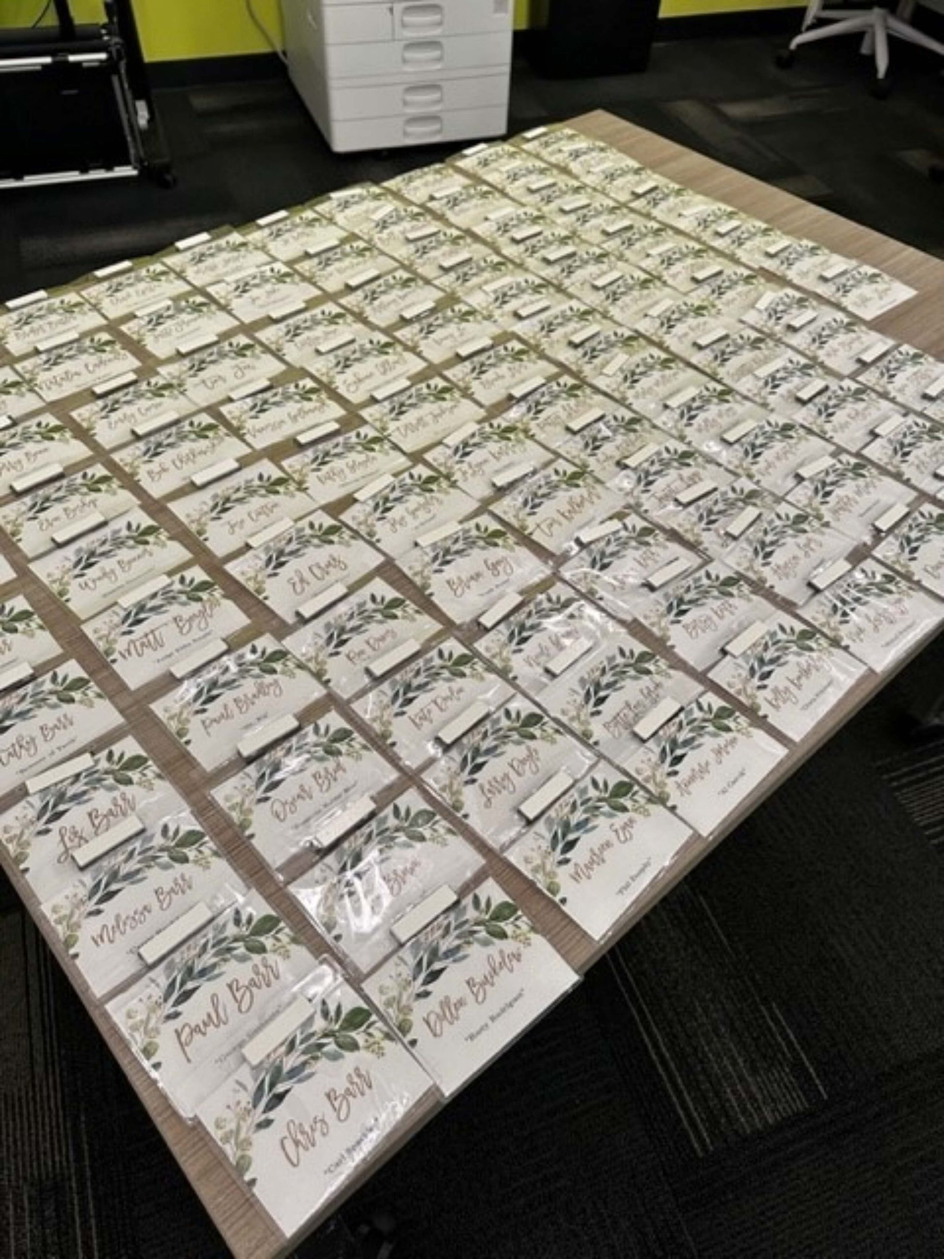 Rows of small white gift boxes with handwritten labels arranged on a table in an office setting