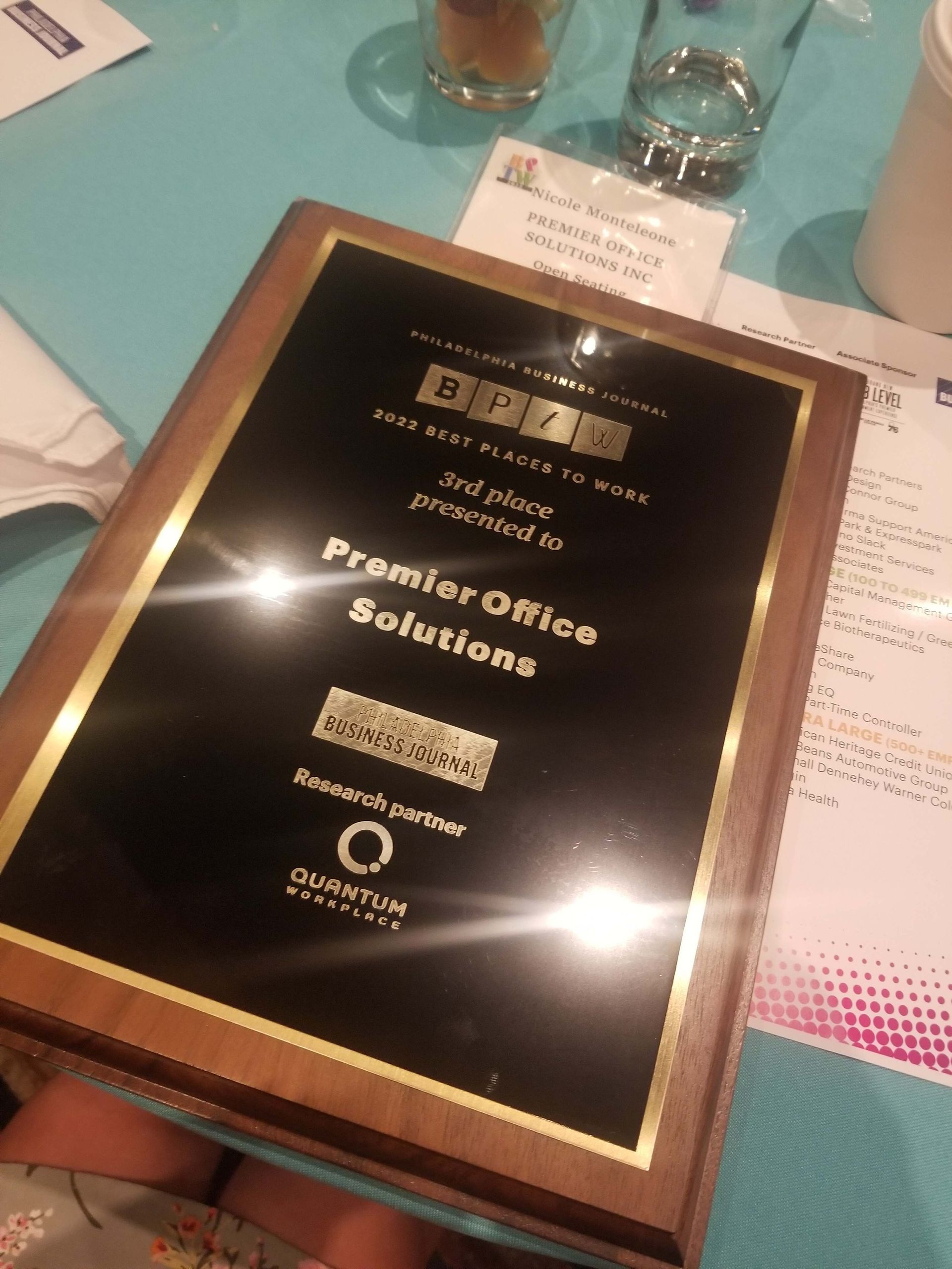 Framed award plaque on a teal table beside drinks and a napkin, labeled “Promotional Solutions”