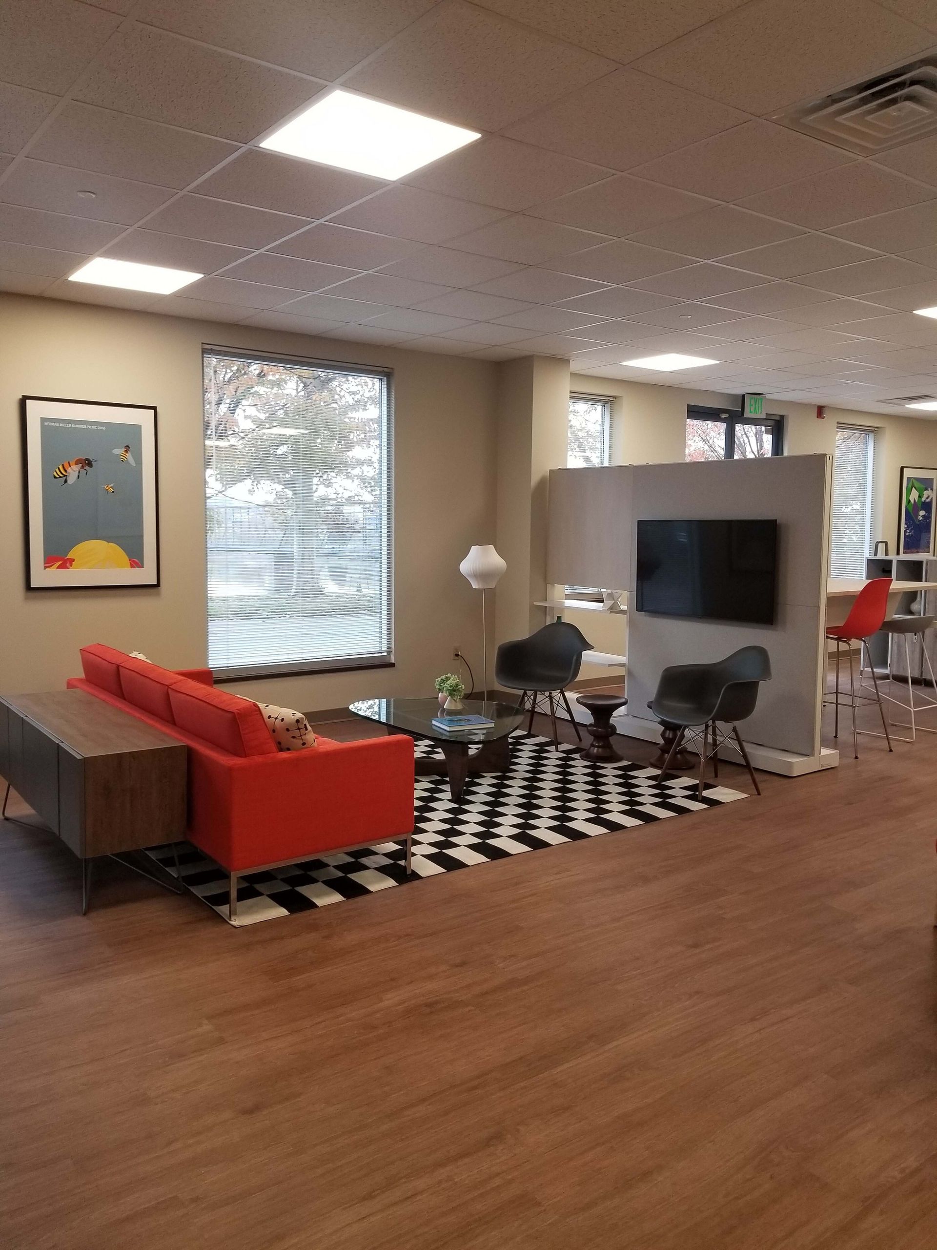 Modern lounge with red sofa, black chairs, TV, patterned rug, and wood flooring in an office lobby
