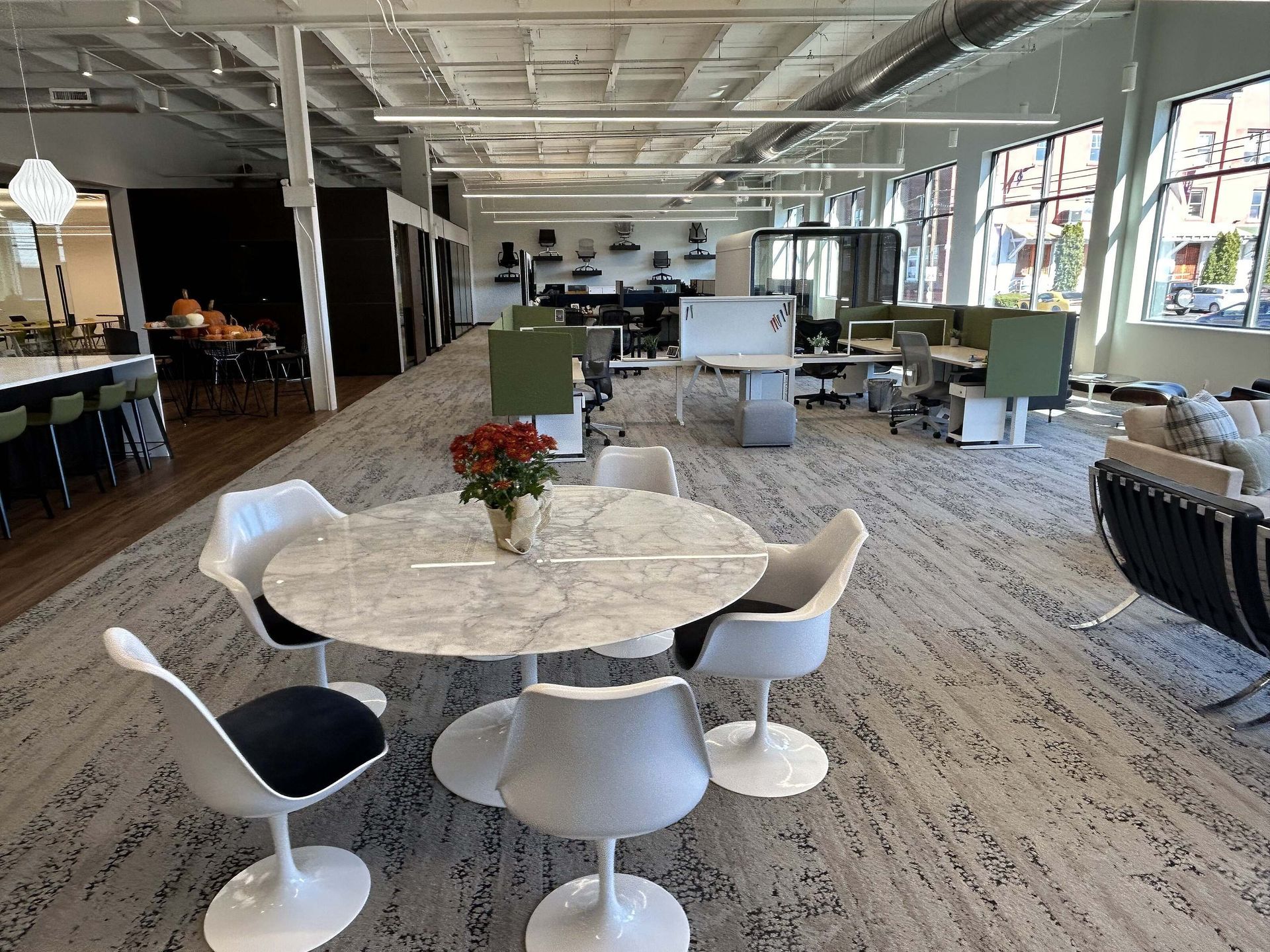 Modern lounge with round white tables, green chairs, and large windows in an open office space