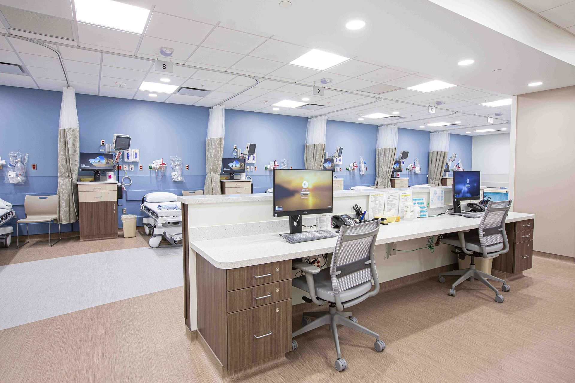Modern hospital nurses’ station with computers, desks, and blue patient care area in the background