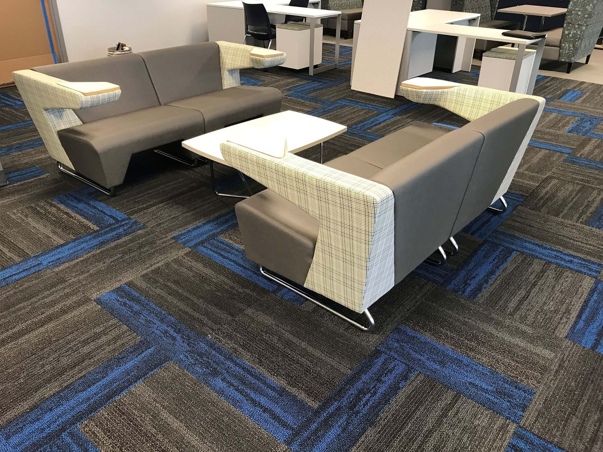 Modern lounge area with gray sofas and cream side tables on a blue patterned carpet.