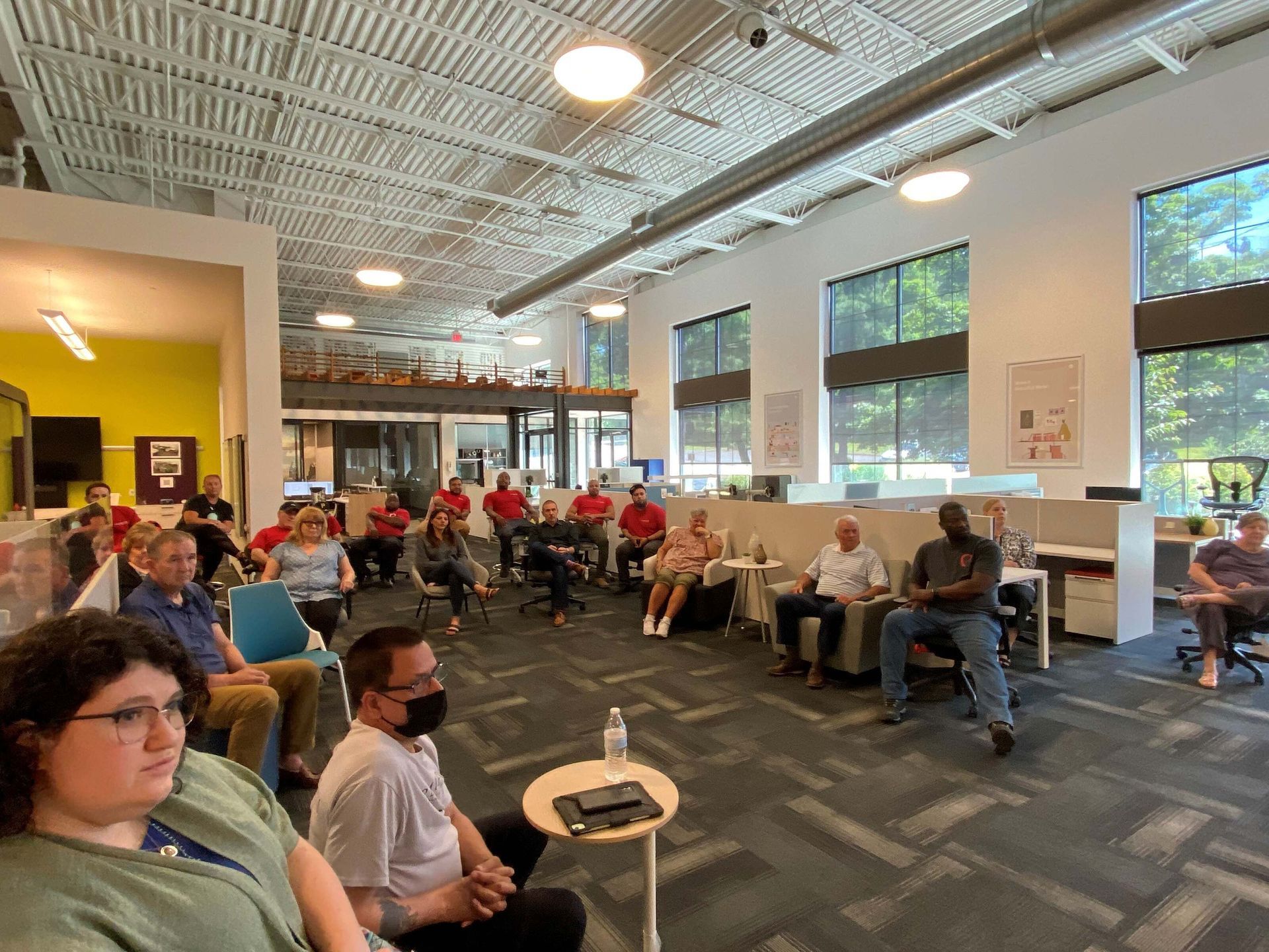 People seated in a bright waiting room with large windows and overhead lights.