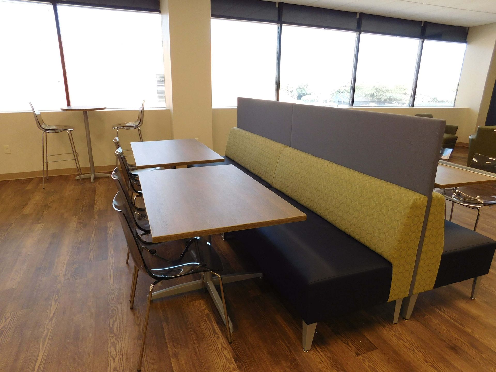 Conference room with long tables, black chairs, and yellow-gray bench seating by large windows.