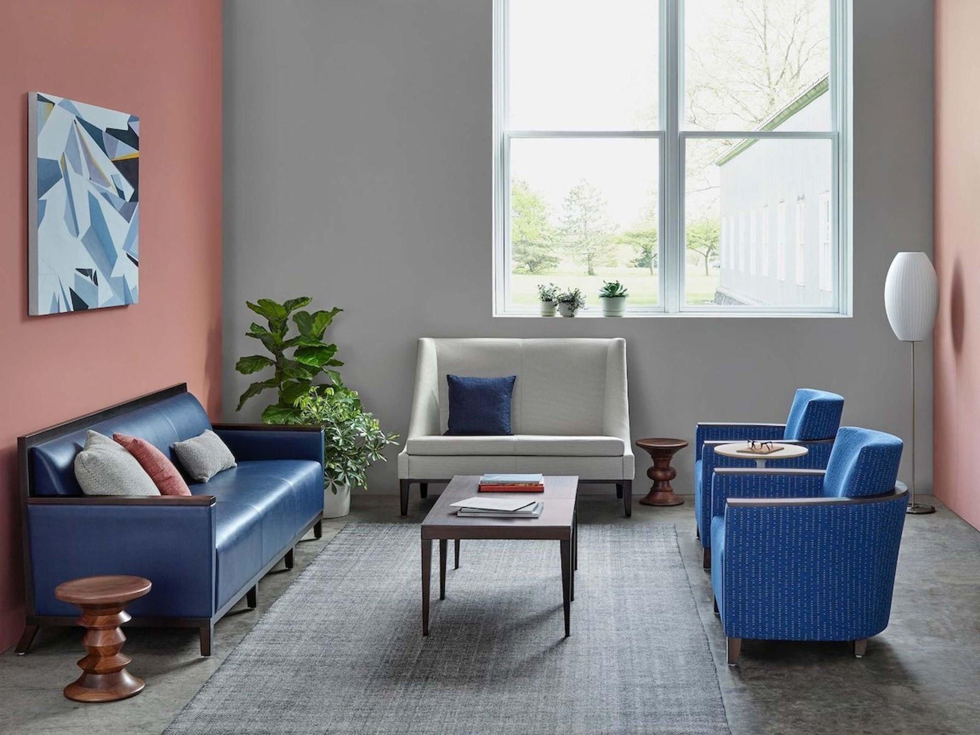 Modern living room with blue and gray seating, coffee table, plant, and abstract wall art.