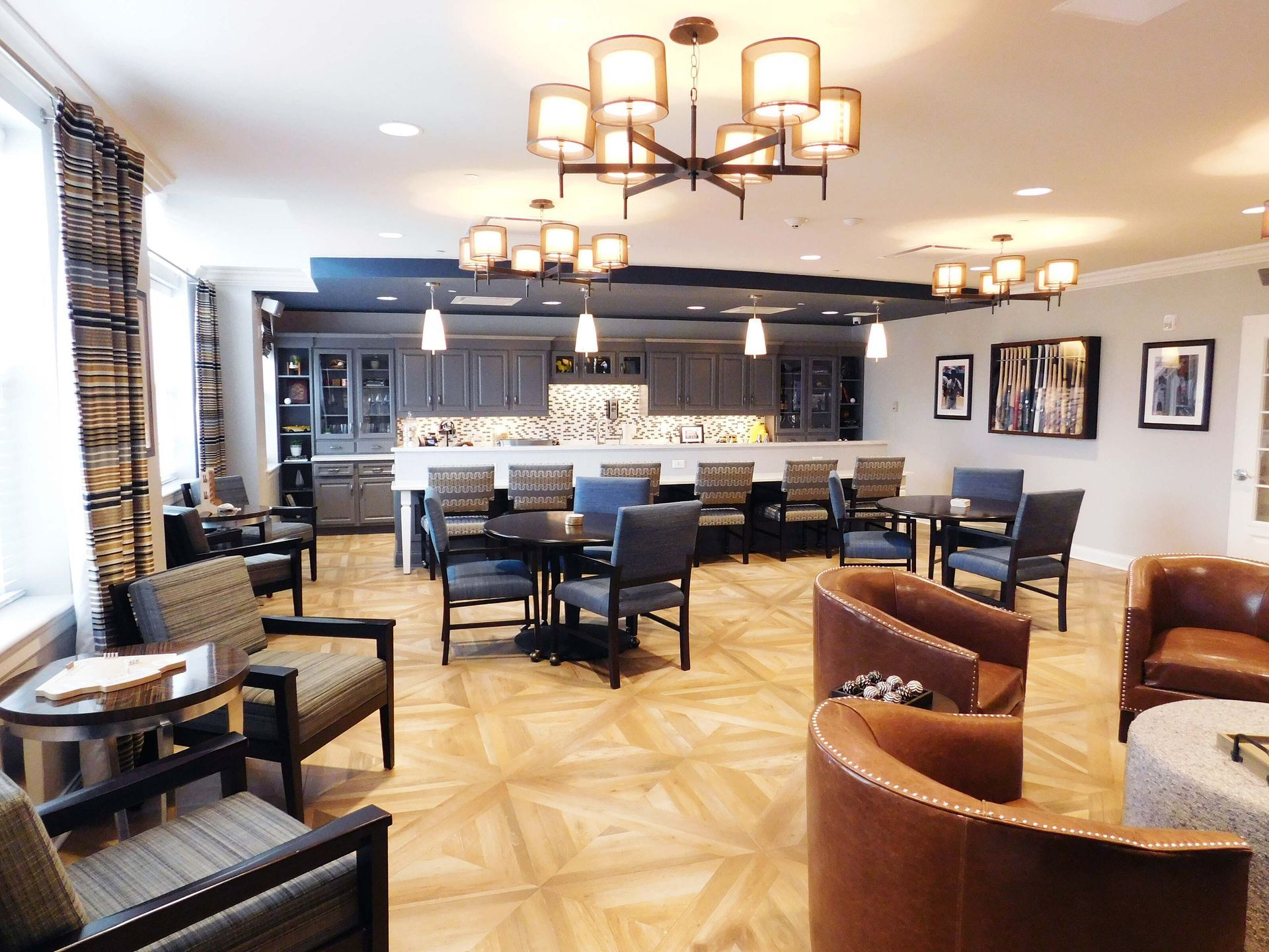 Elegant lounge with blue chairs, brown armchairs, chandeliers, and a marble bar in a bright modern room
