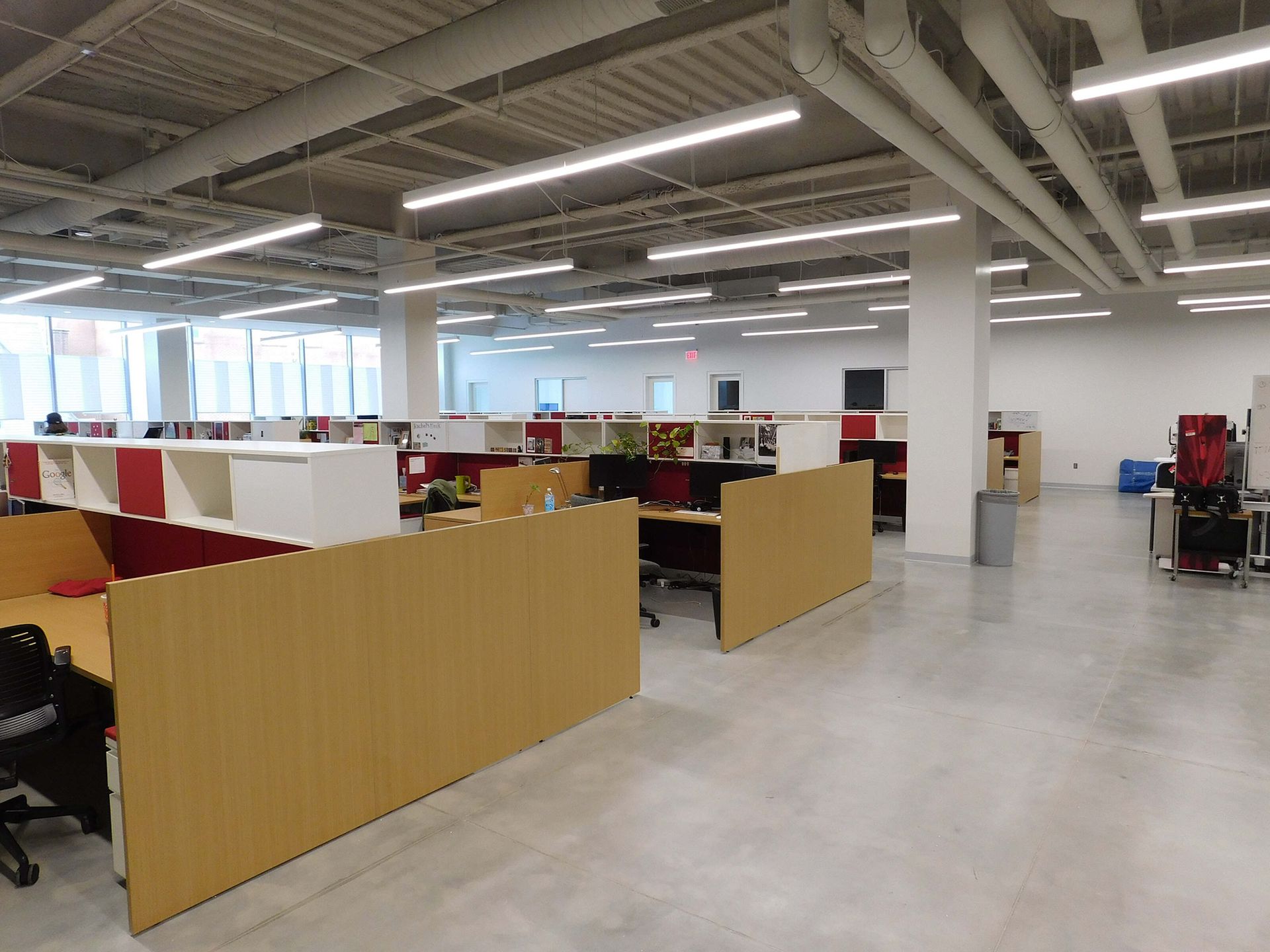 Open office workspace with tan cubicles, desks, and overhead fluorescent lights