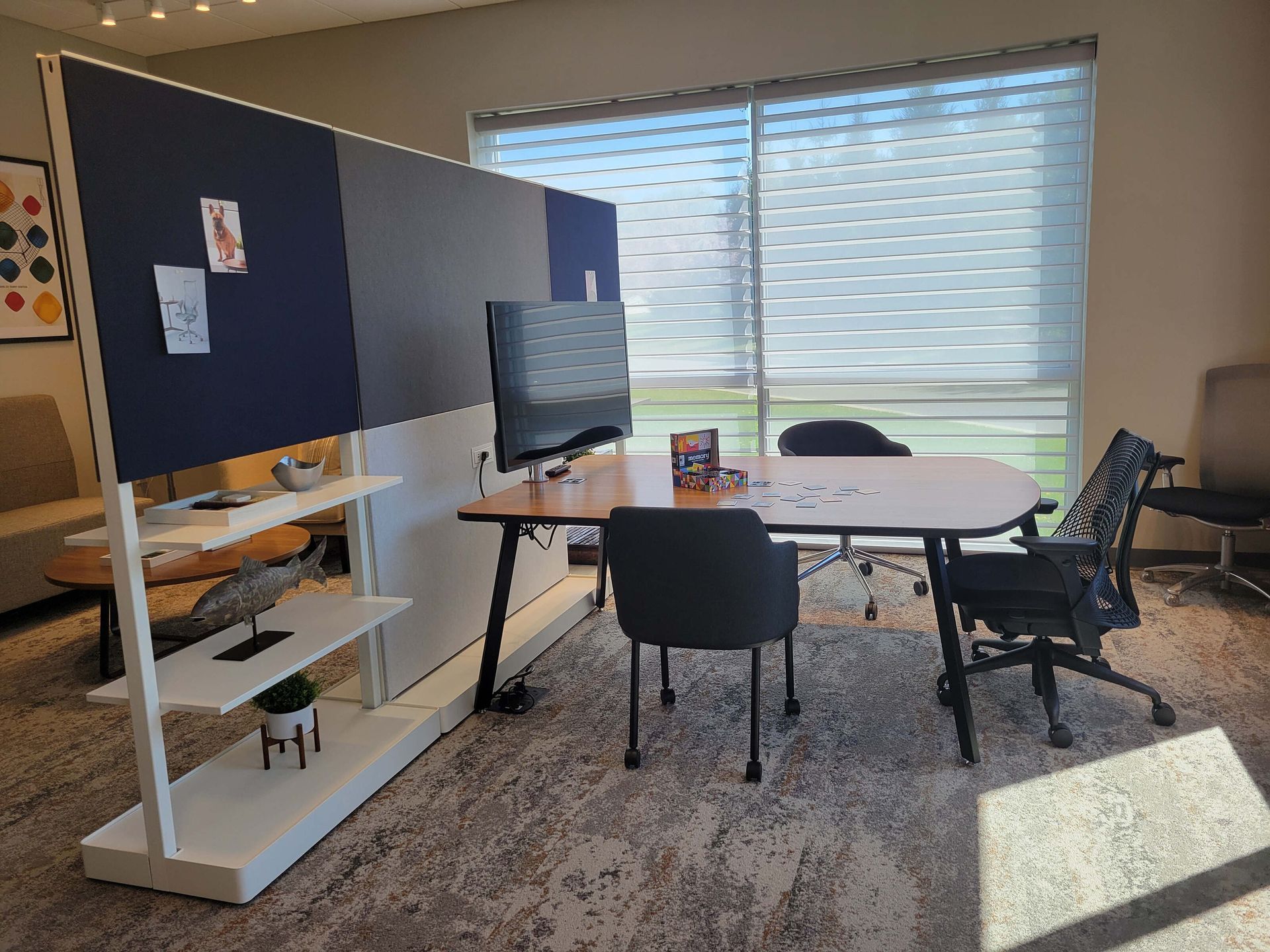 Small meeting room with desk, chairs, TV monitor, and large window with blinds.