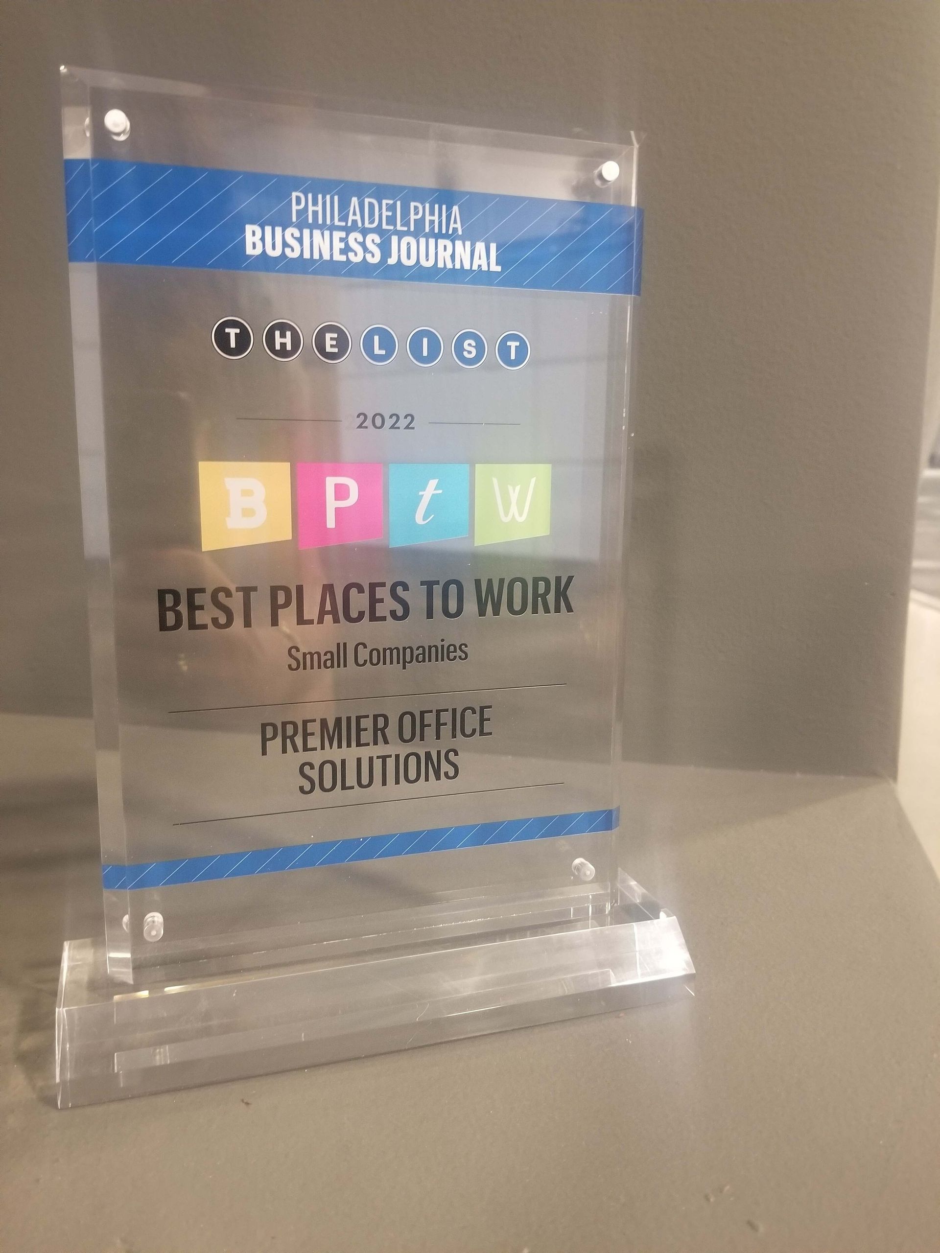 Clear acrylic award plaque with blue and multicolored text on a shelf.