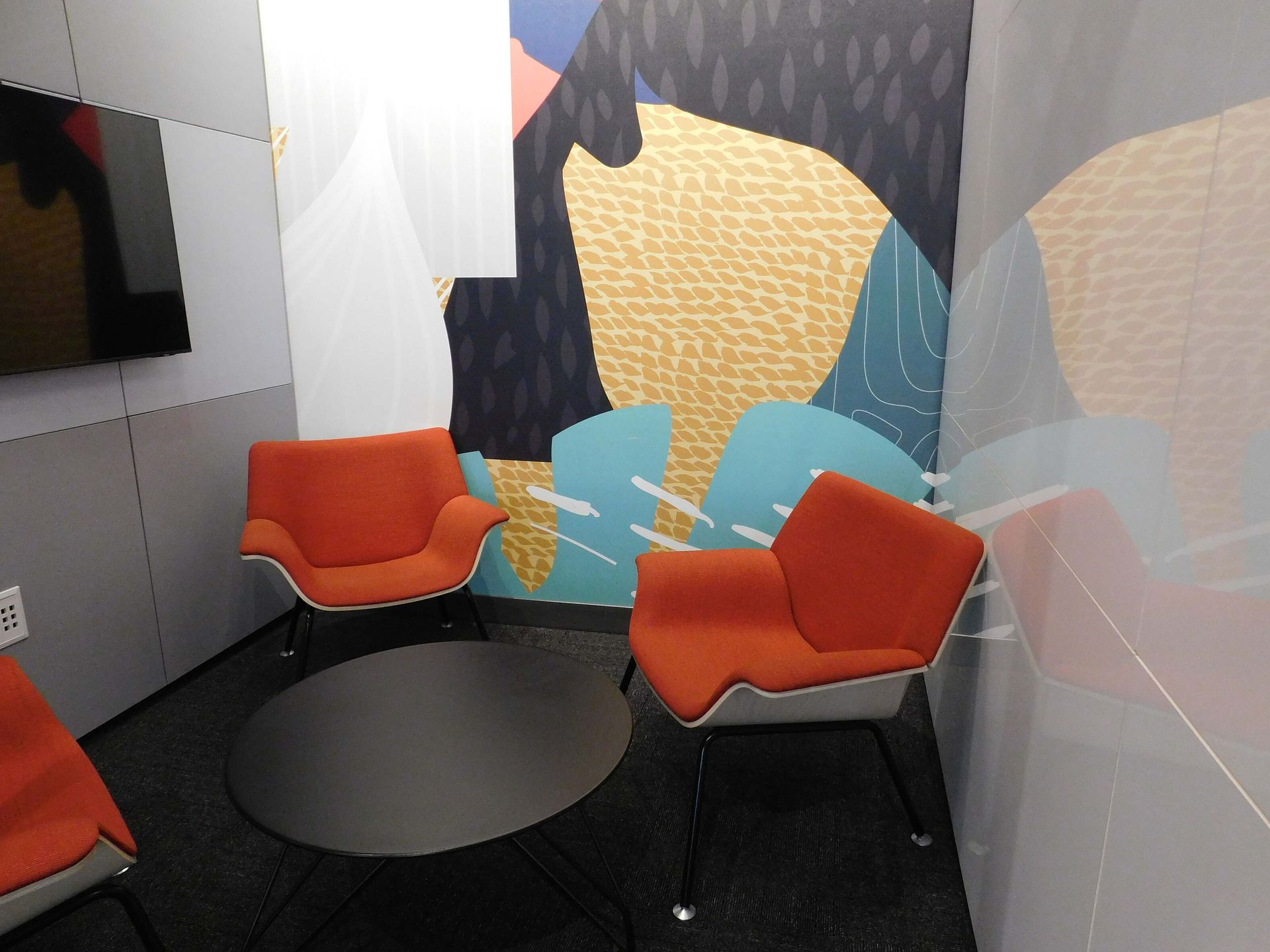 Small lounge with two orange chairs, a round black table, and patterned wall panels.