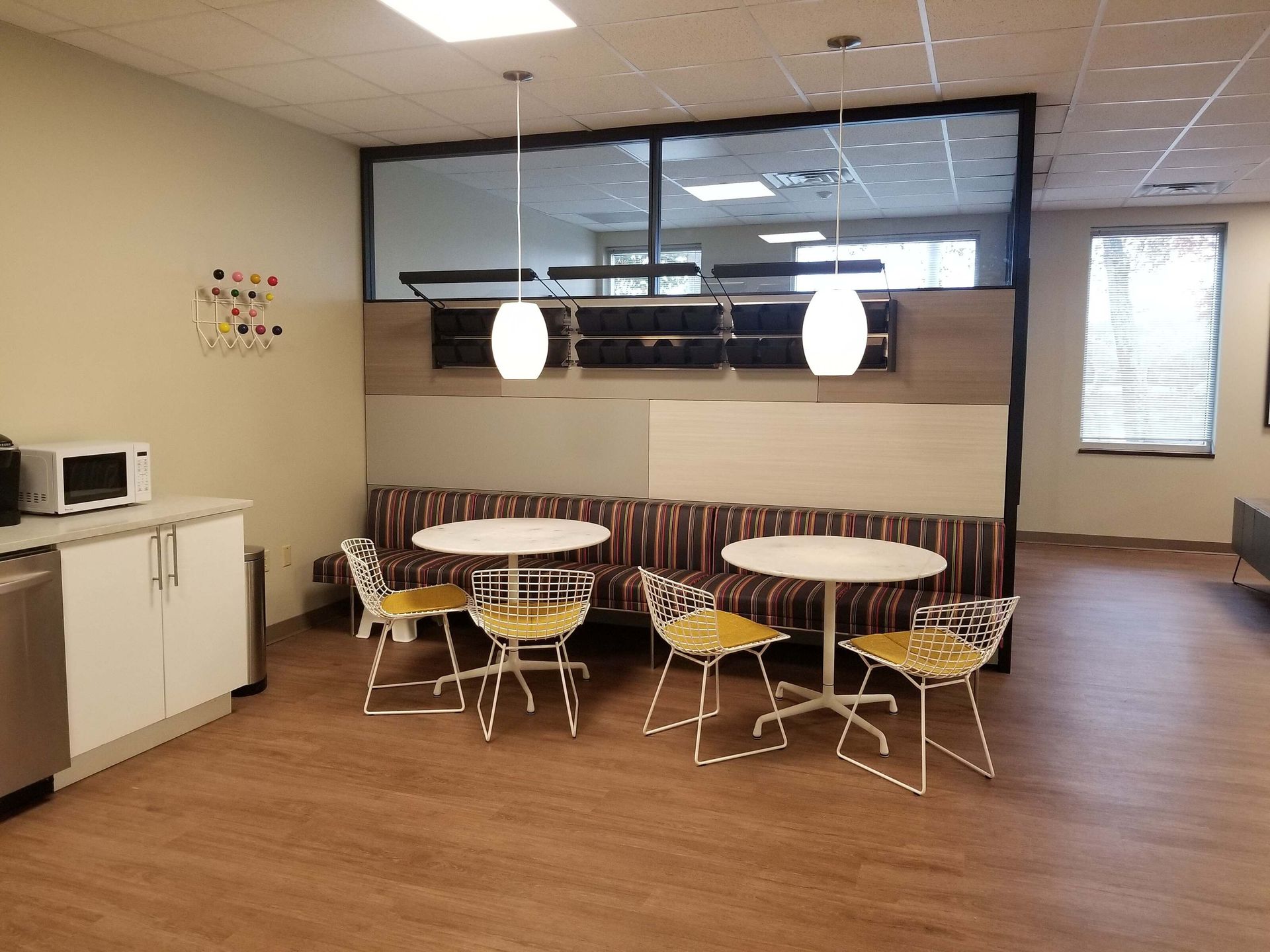 Small break room with round tables, yellow chairs, kitchenette, and large interior window