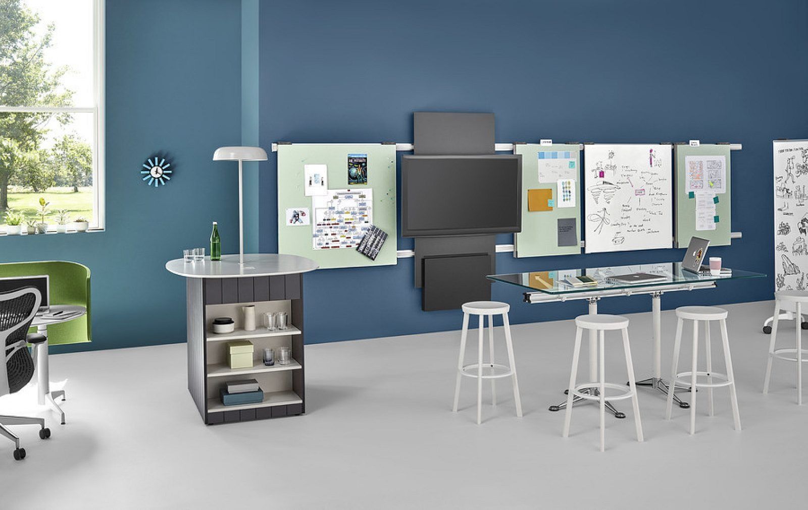 Modern office workspace with blue walls, desks, stools, shelves, and pinned notes on display boards