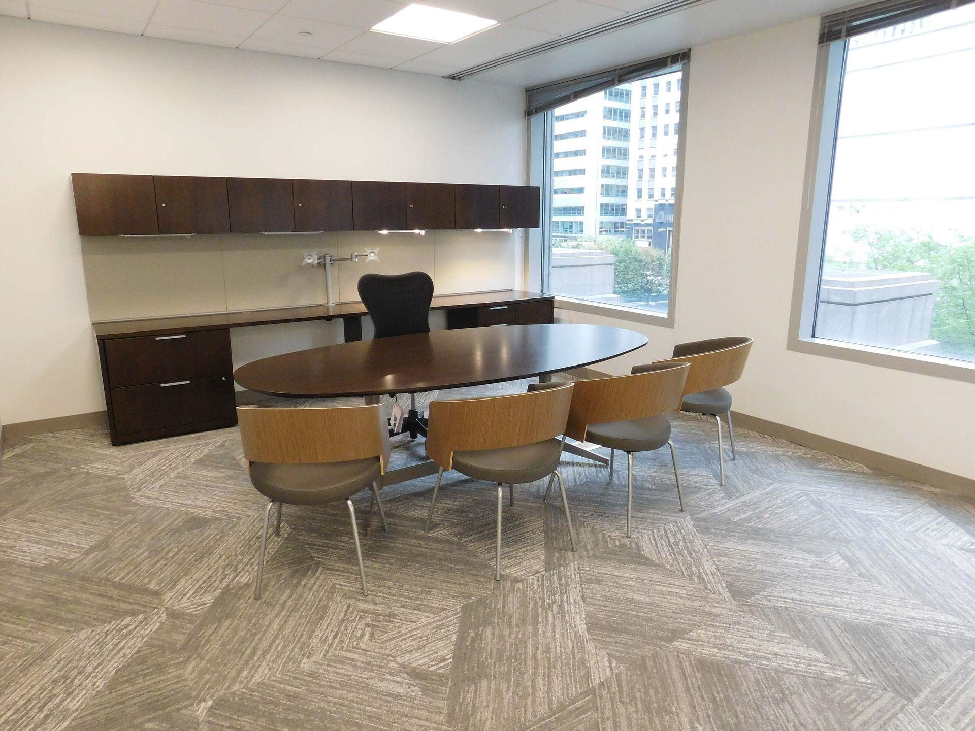 Modern office conference room with oval table, brown chairs, cabinets, and large windows