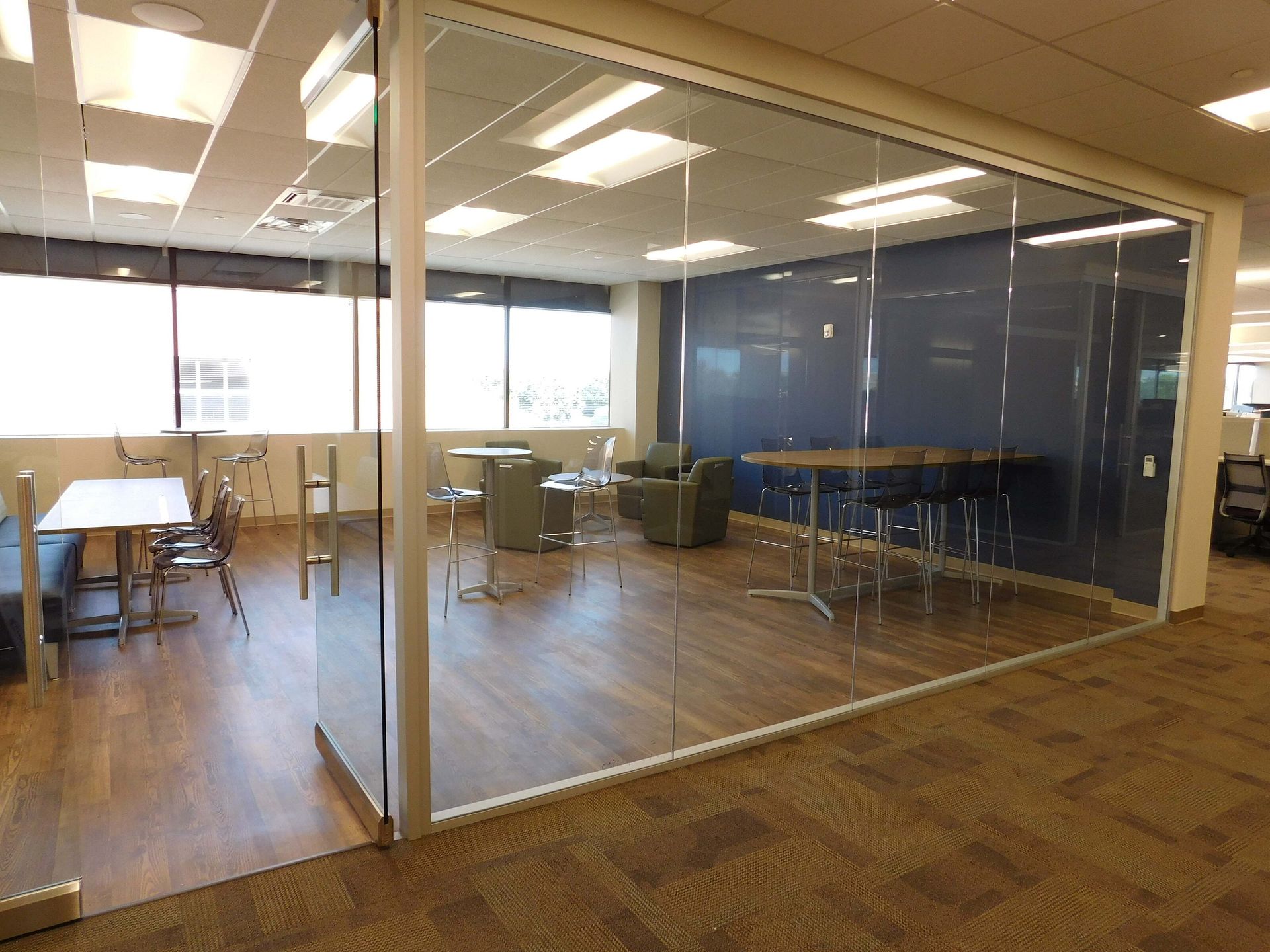 Modern office lounge with glass walls, wood floors, tables, chairs, and blue accent wall