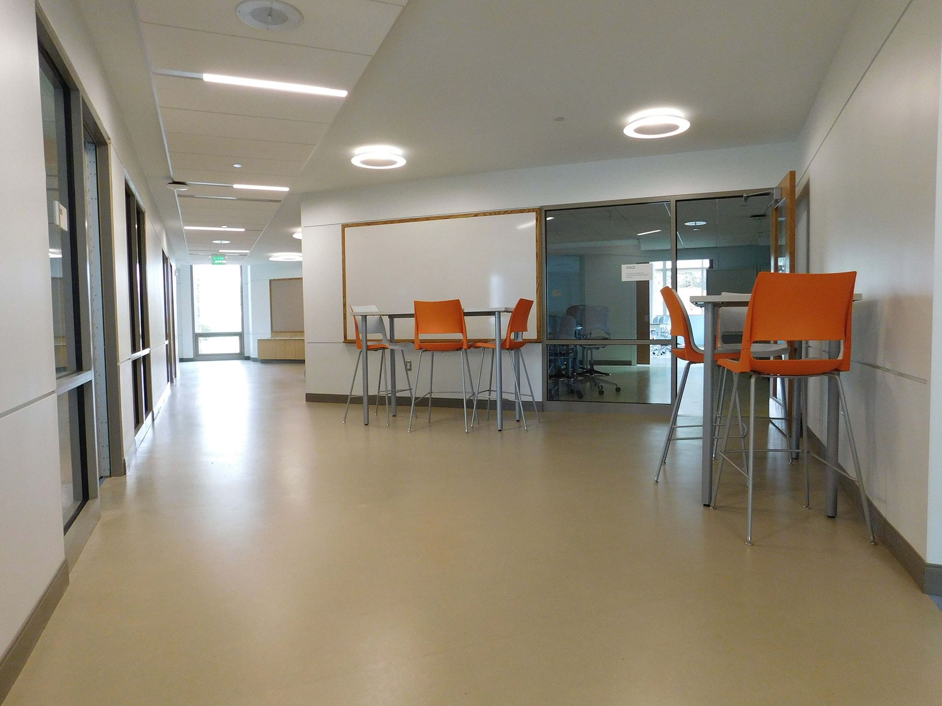 Empty modern office hallway with orange bar stools and tables by glass walls