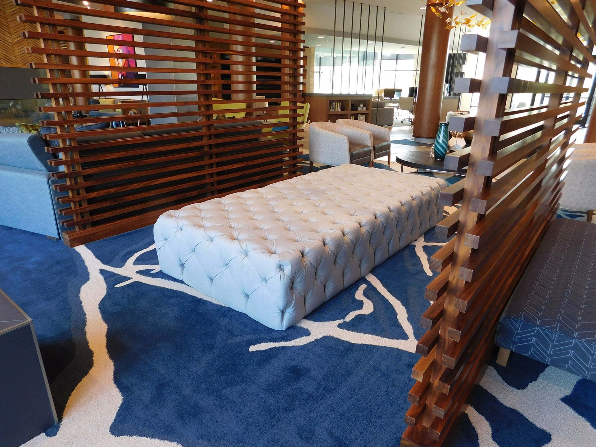 Modern lounge with tufted ottoman, blue patterned rug, and wooden slat partitions
