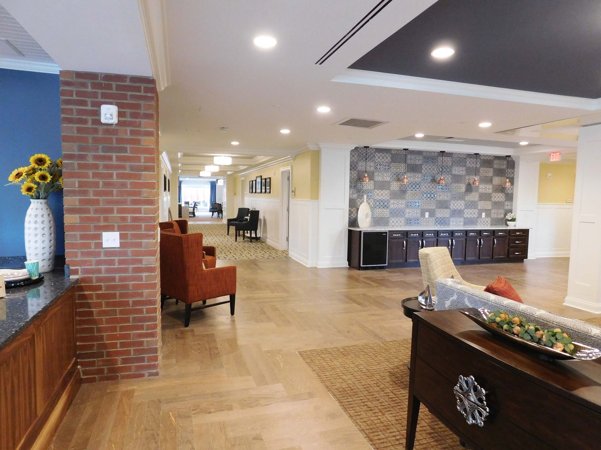 Bright lobby with brick wall, seating area, wood floor, and buffet table under recessed lighting