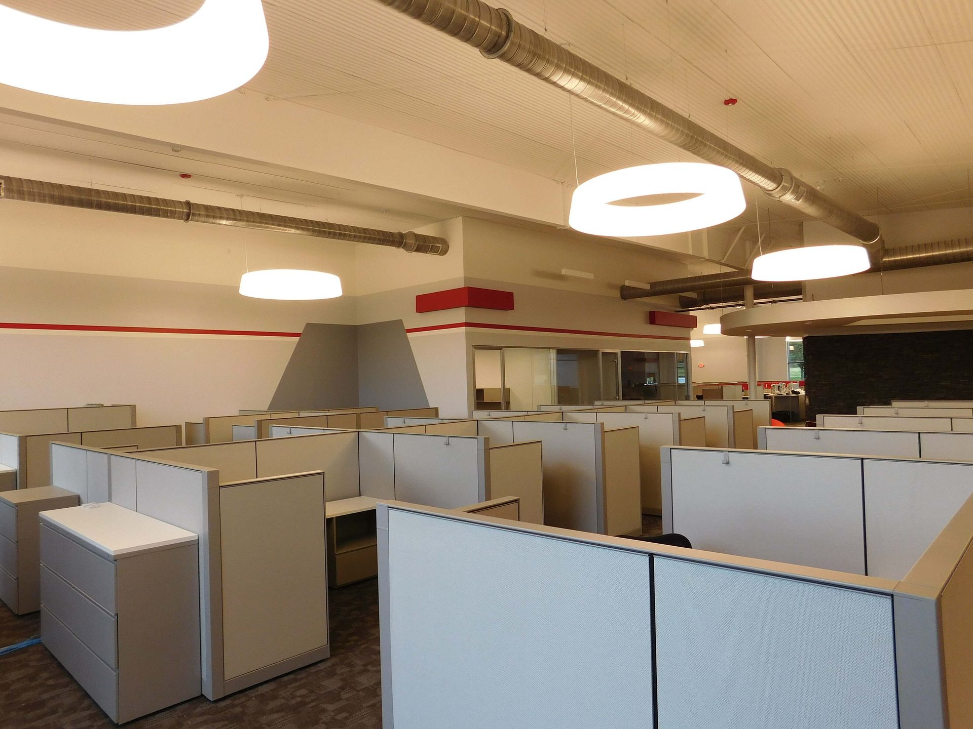 Open office cubicles with beige partitions and overhead lights, no people visible.