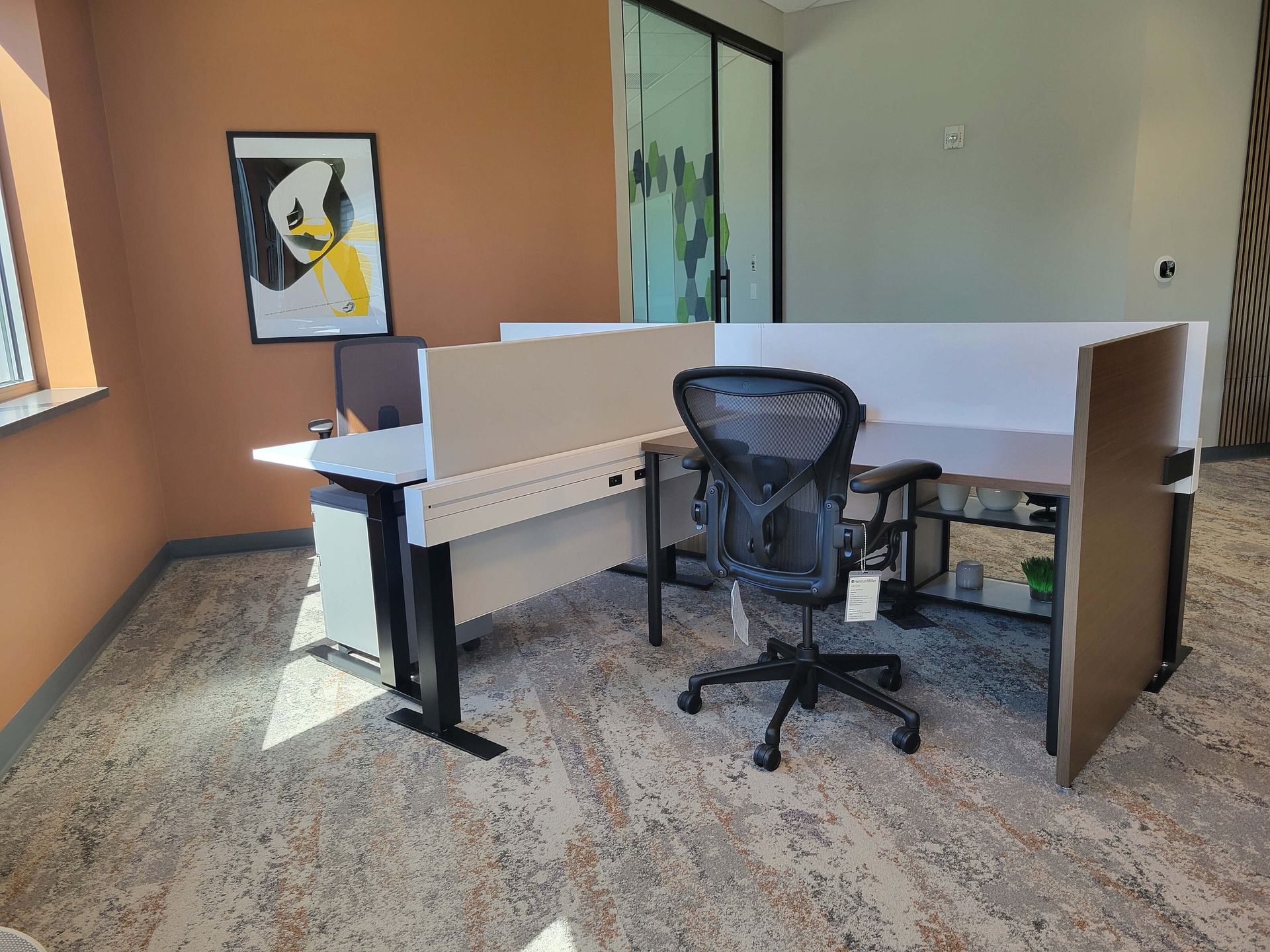 Office cubicle with a black chair, desk, and partition walls in a small room.