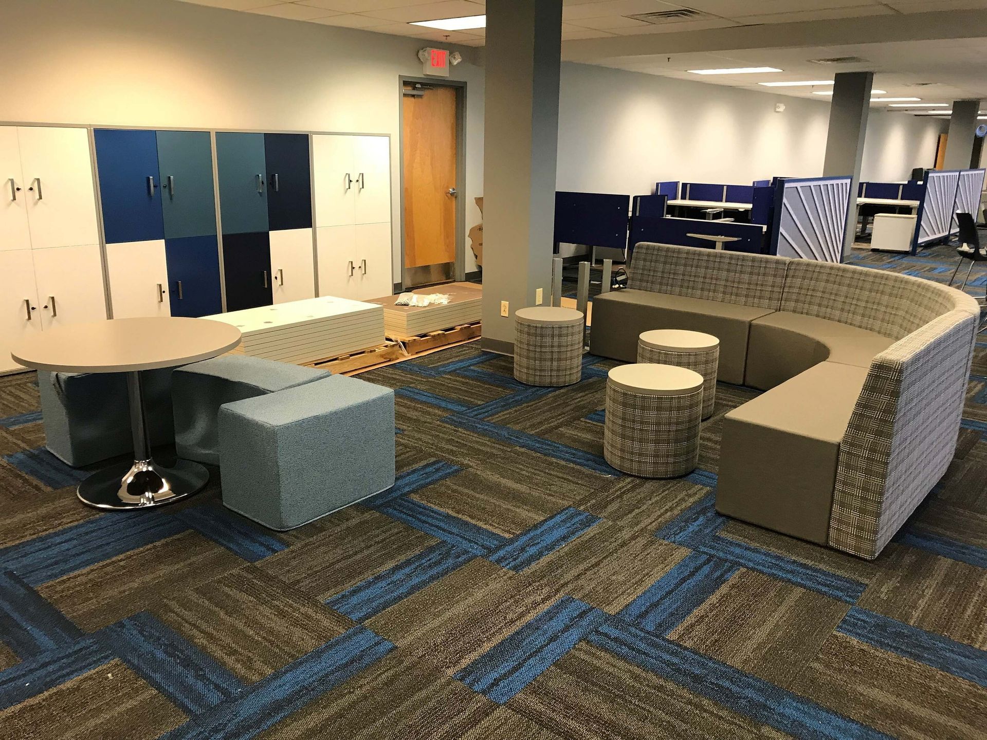 Modern lounge area with blue carpet, curved booths, round tables, and lockers along the wall
