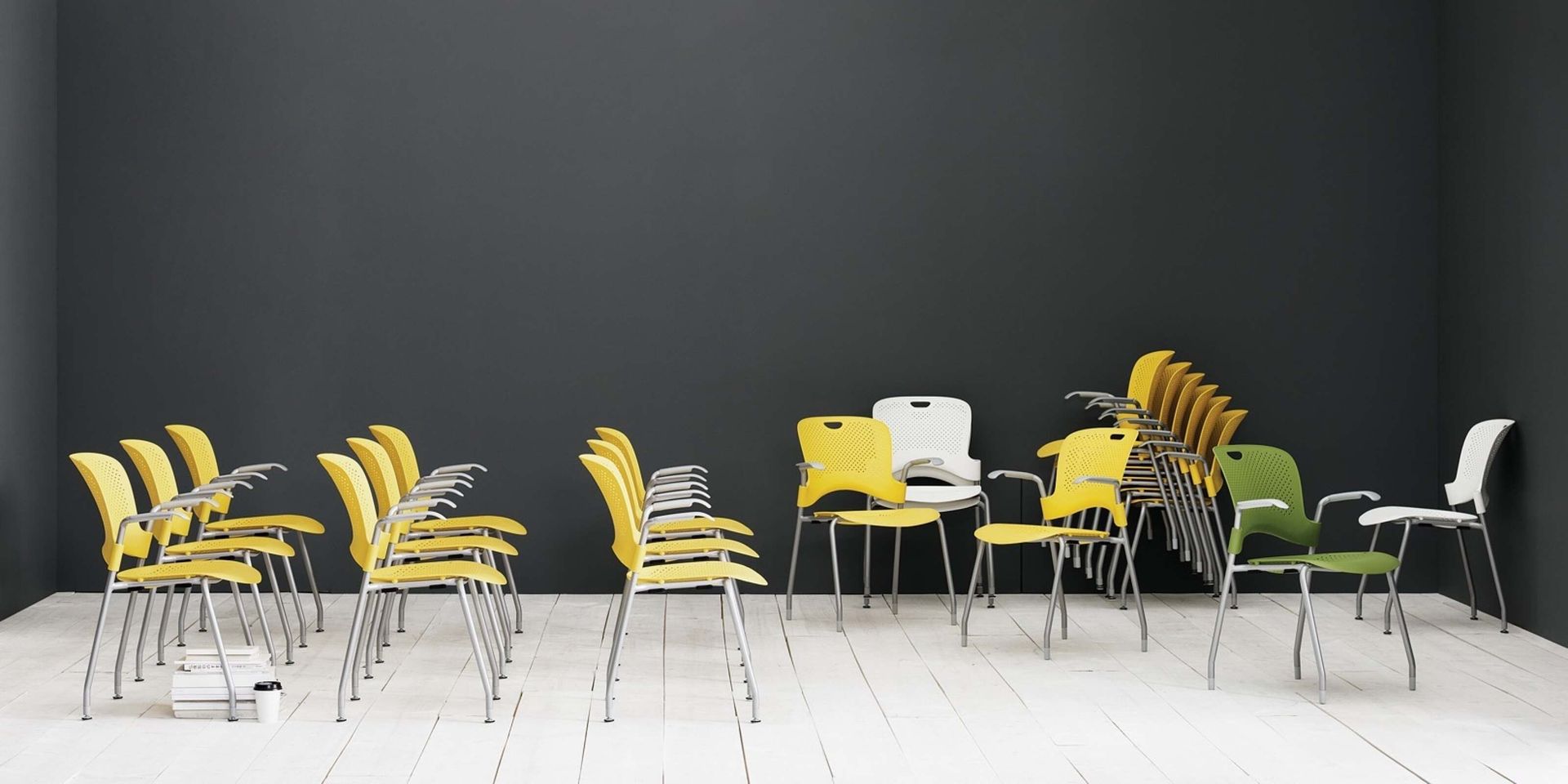 Rows of yellow and white chairs in an empty modern room with a dark wall