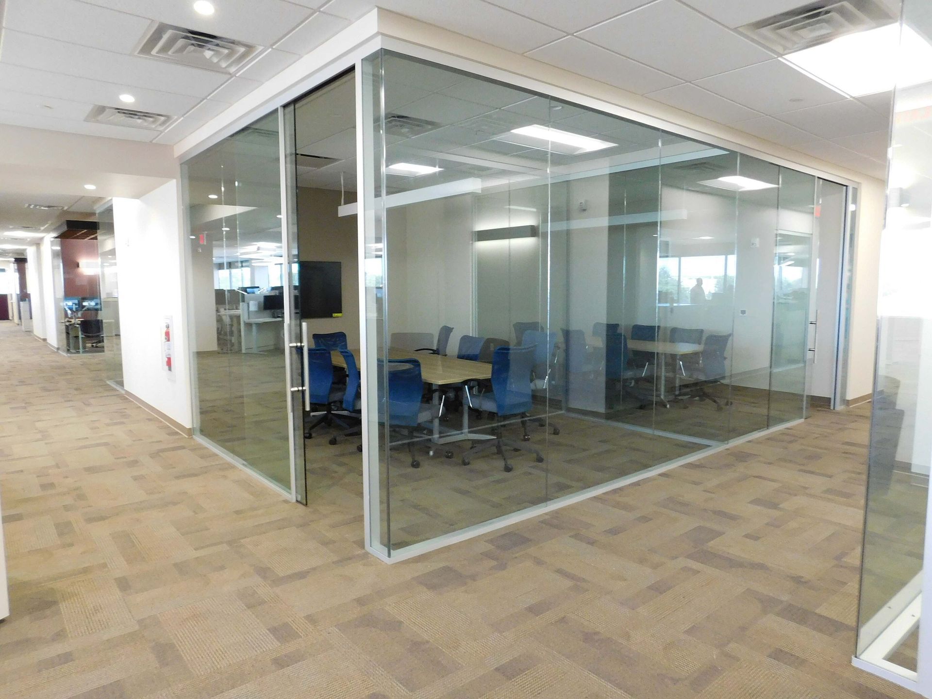 Glass-walled conference room with blue chairs in a modern office hallway