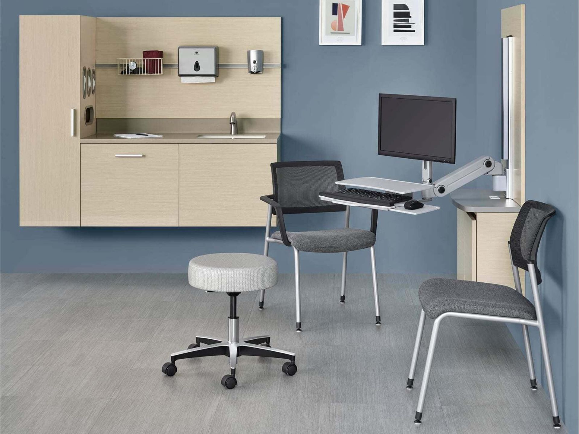 Accessible exam room with adjustable desk, stools, cabinets, and wall-mounted equipment.