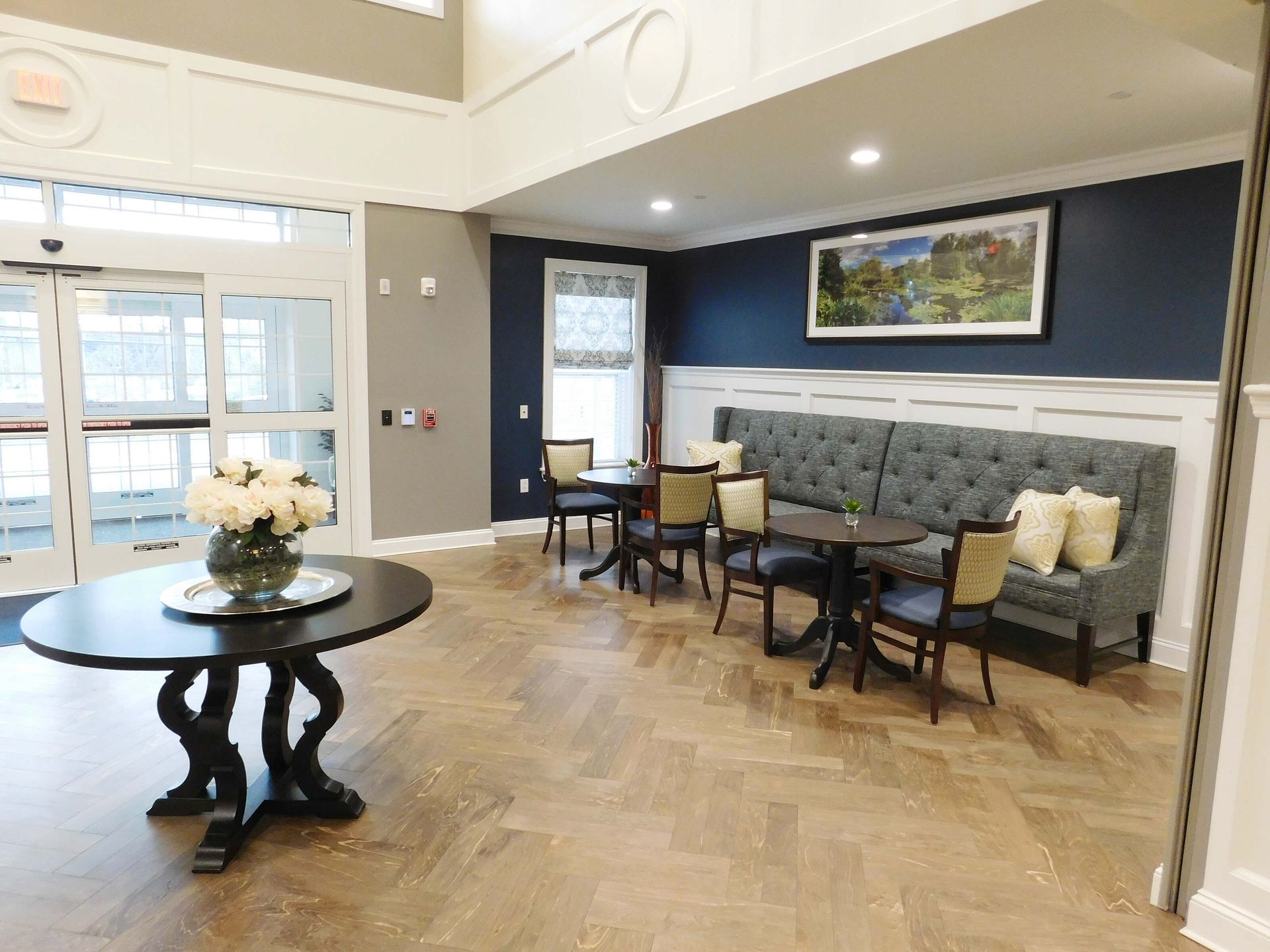 Bright lobby with round table, chairs, cushioned bench, and wall art on wood floor