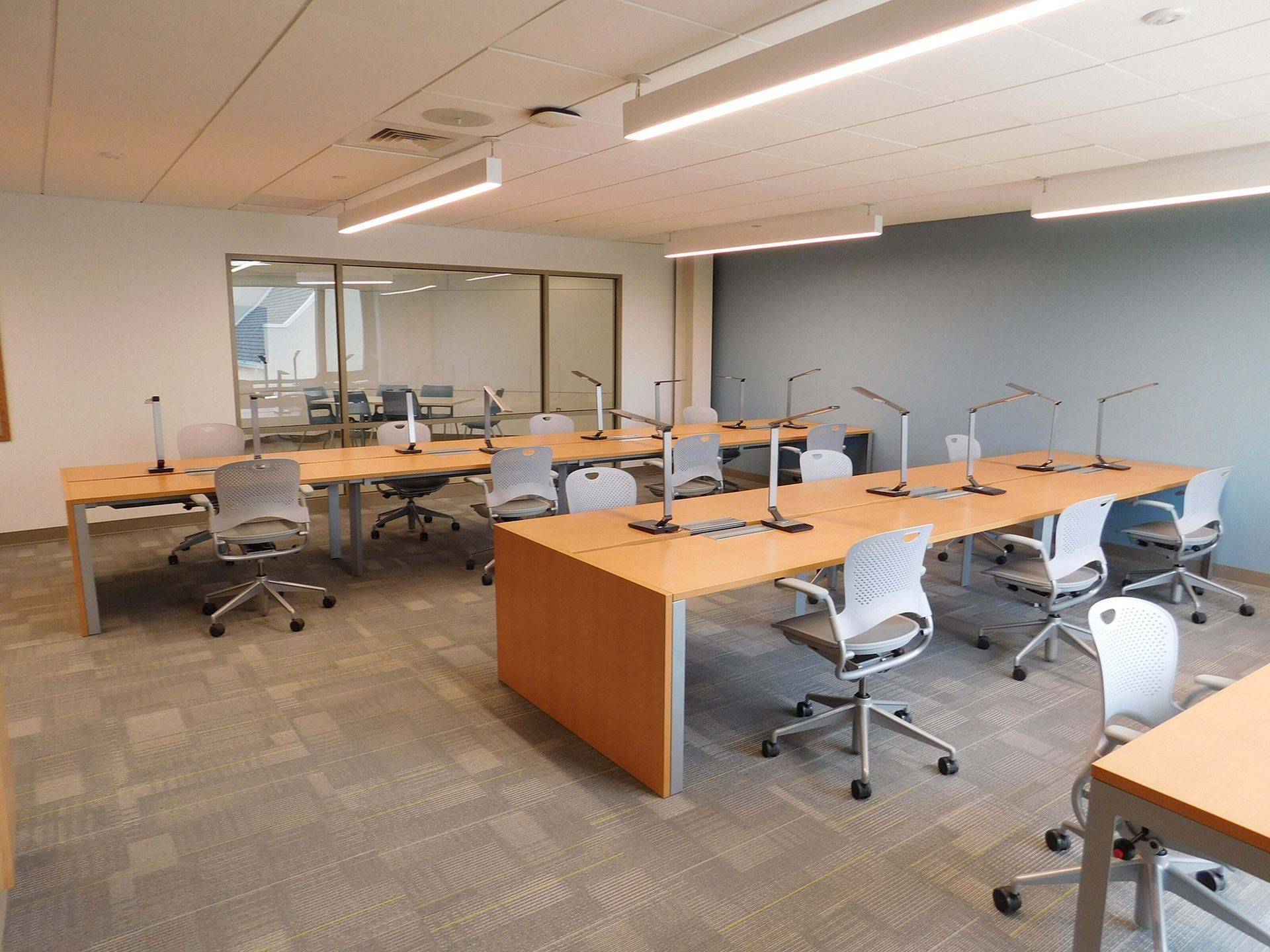 Empty modern office with desks, rolling chairs, and glass-walled meeting room
