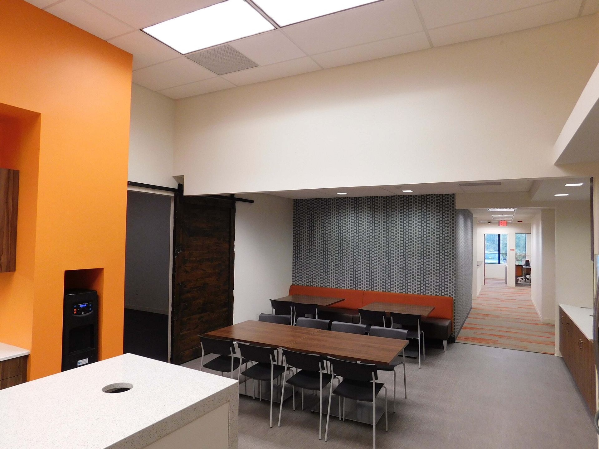 Empty modern room with tables, orange wall, patterned curtain, and hallway opening in back