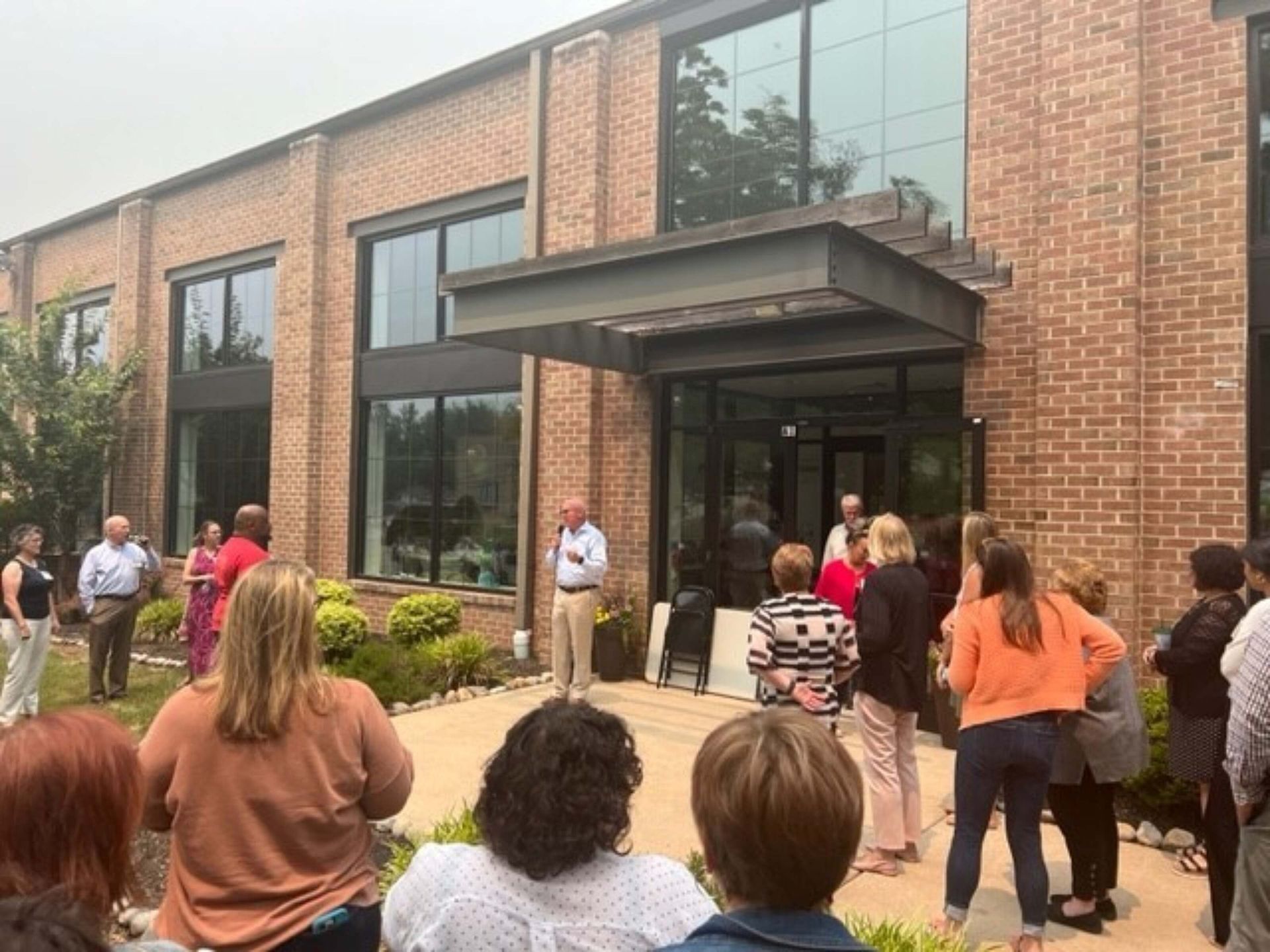 People gathered outside a brick building entrance under a glass awning.