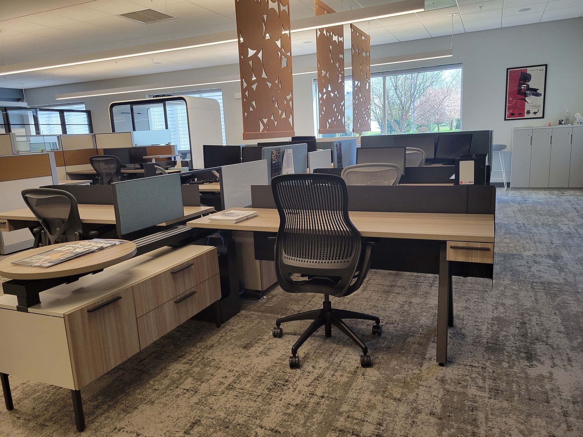 Open office with desks, monitors, and black chairs under bright overhead lighting.