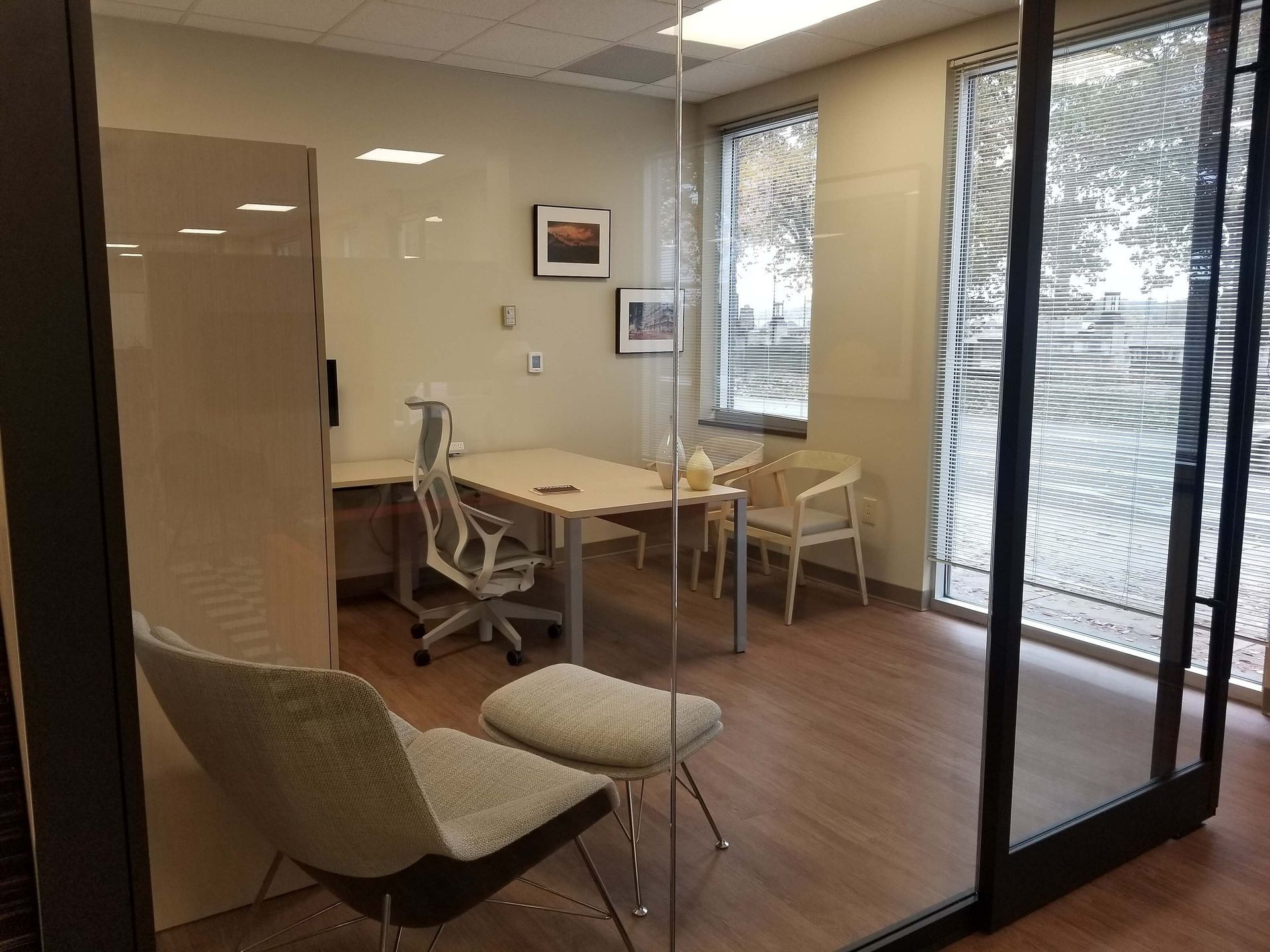 Empty waiting room with chairs, desk, and large windows beside a glass door