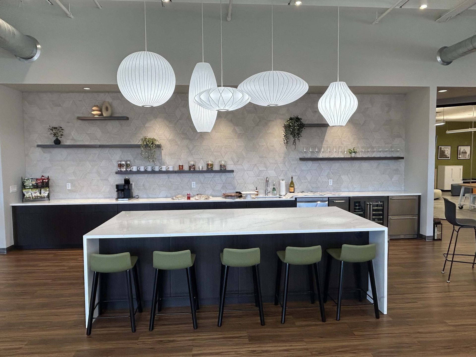 Modern kitchen with large island, green stools, pendant lights, and wood floors