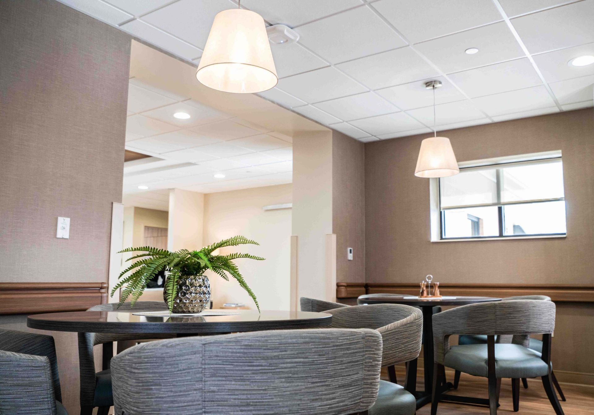 Modern lobby seating area with gray chairs, tables, plants, and hanging pendant lights