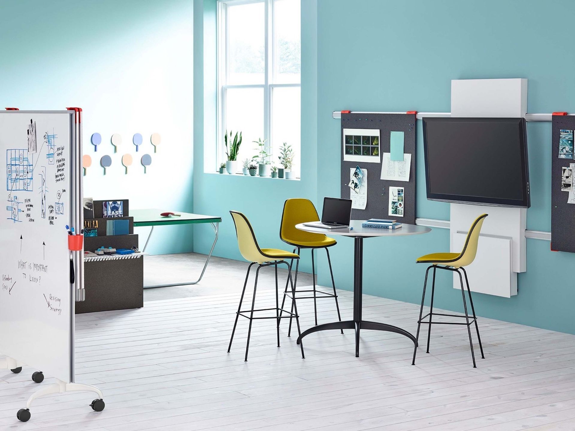 Bright classroom with desks, chairs, a whiteboard, and a large window on teal walls