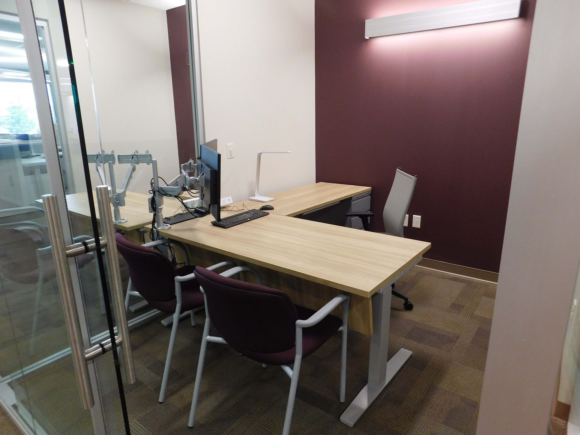 Modern meeting room with wooden table, chairs, and computer monitor beside a glass wall