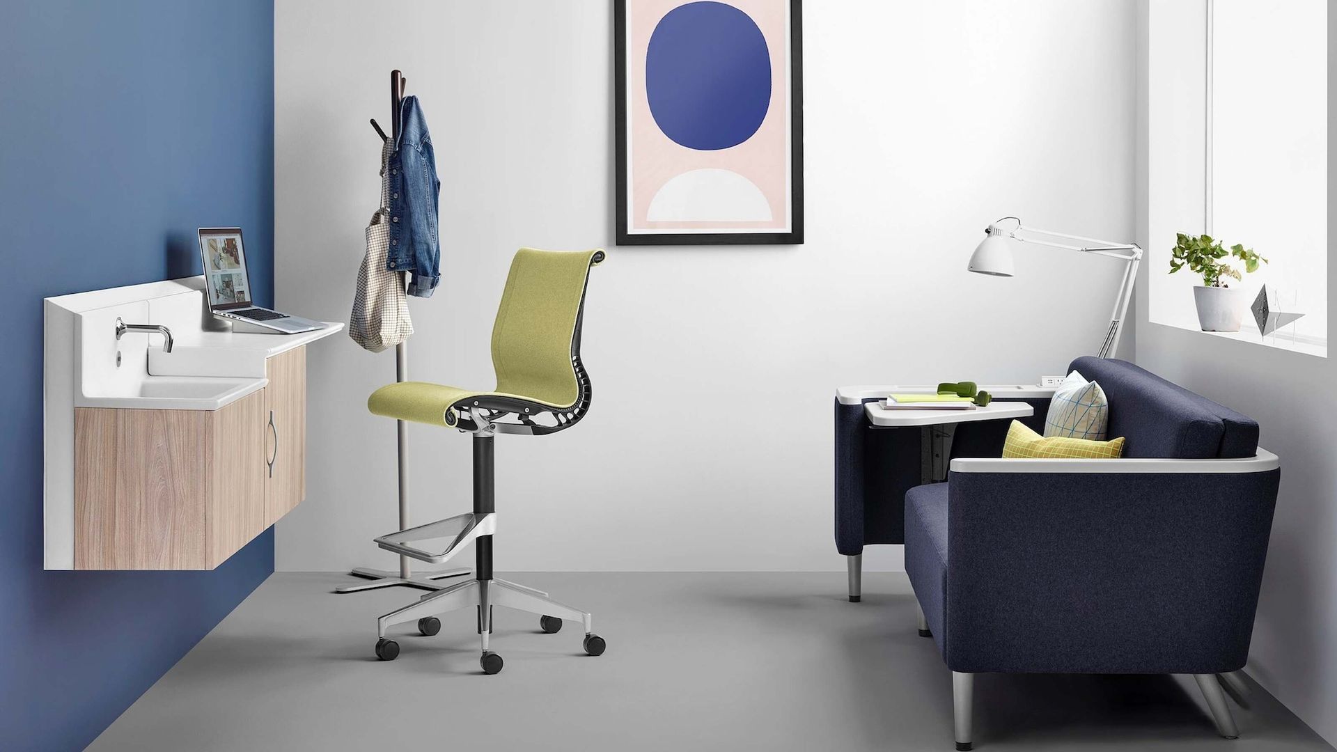 Modern home office with desk, green chair, navy sofa, wall art, and a small cabinet.