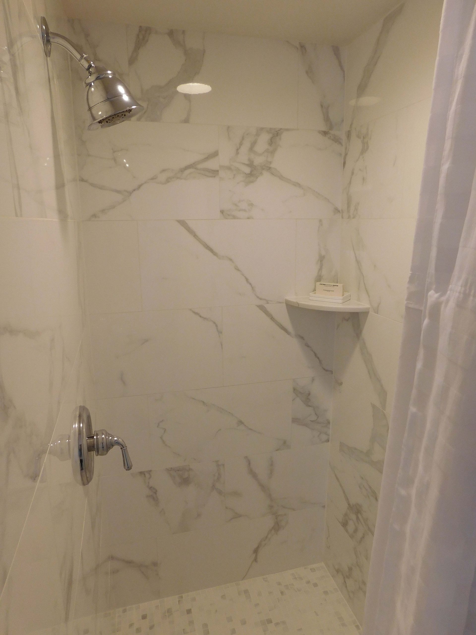 Marble-tiled walk-in shower with chrome showerhead, faucet, and corner shelf