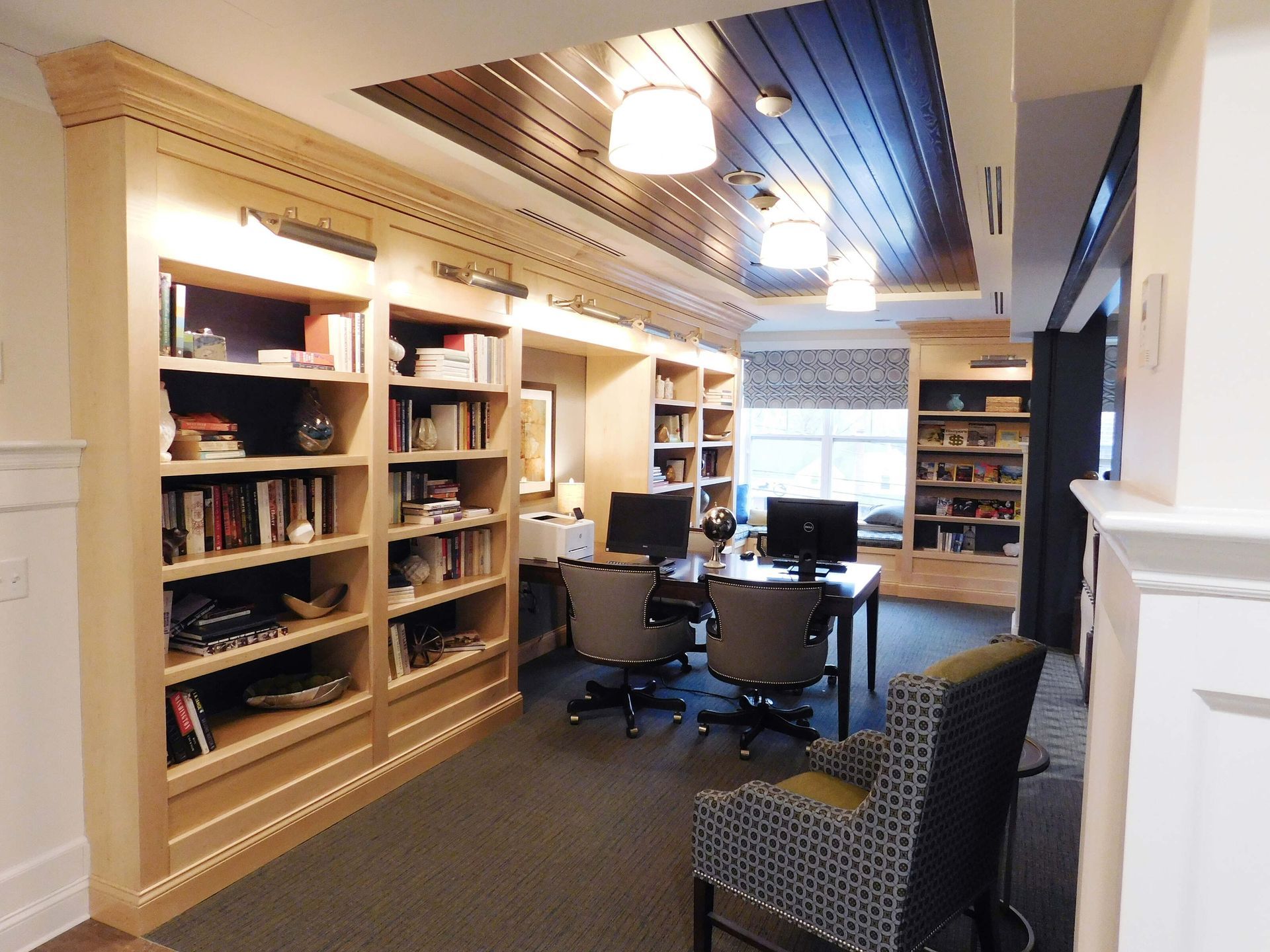Library study room with bookshelves, desks, computers, and chairs under warm ceiling lights