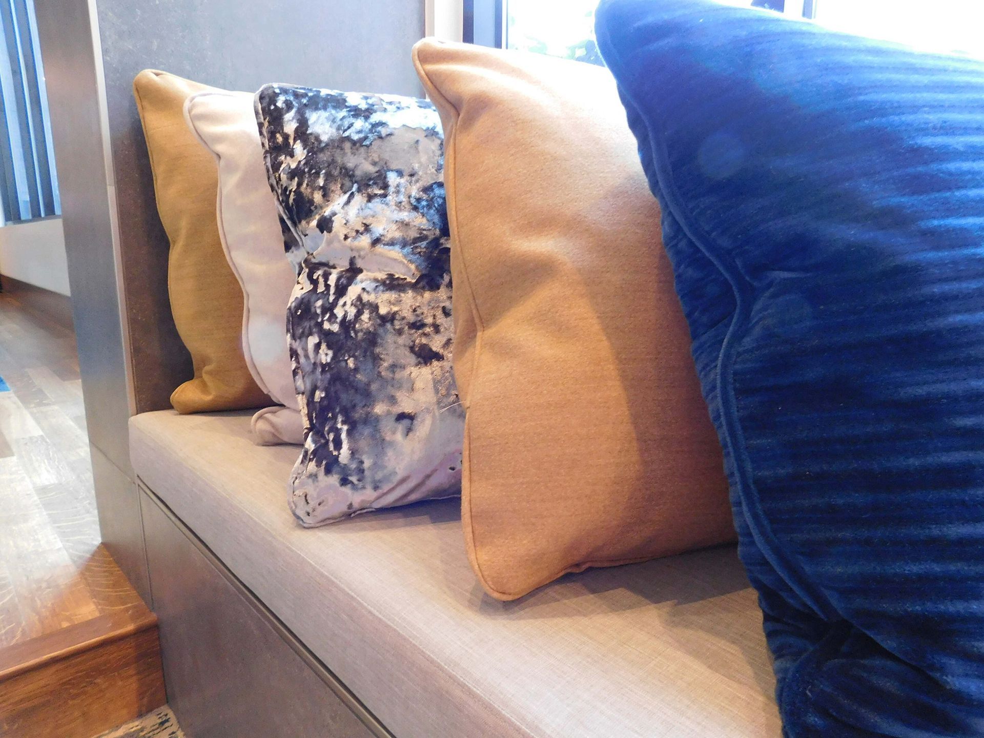 Row of decorative throw pillows in tan, blue, and patterned fabrics on a gray bench