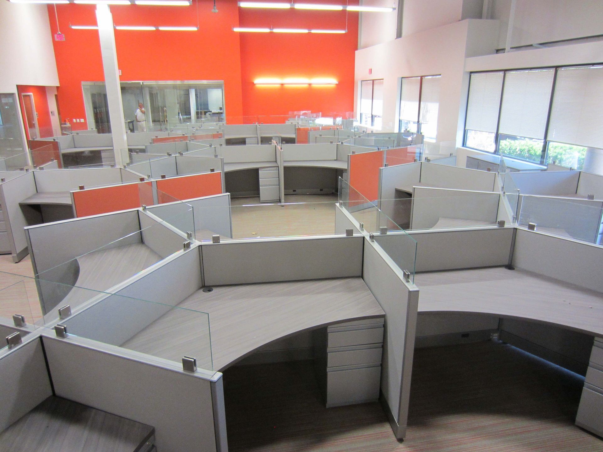 Empty office cubicles in a bright workspace with orange walls and large windows