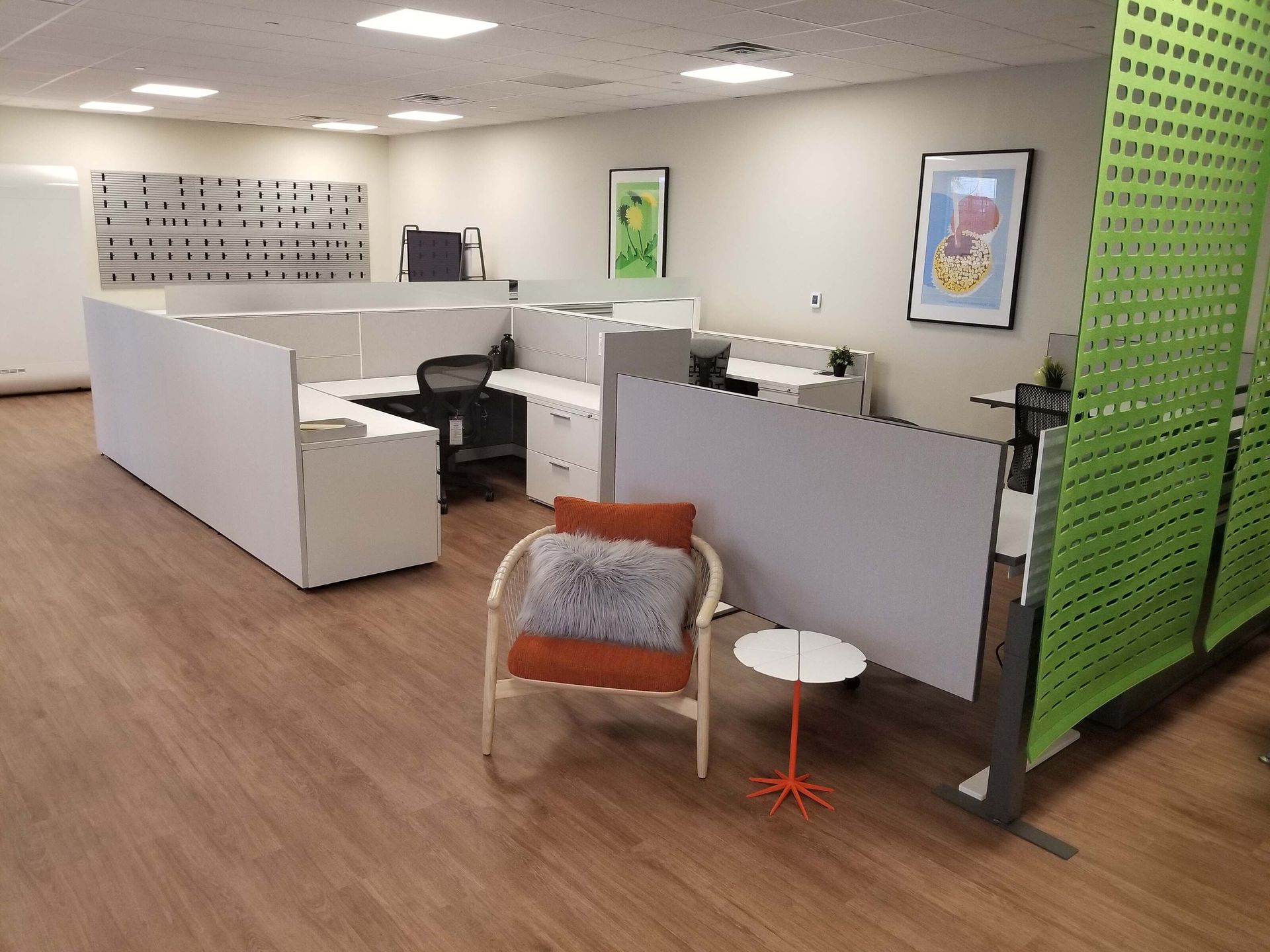 Open office with cubicles, wood floors, orange chair, and a green partition wall.