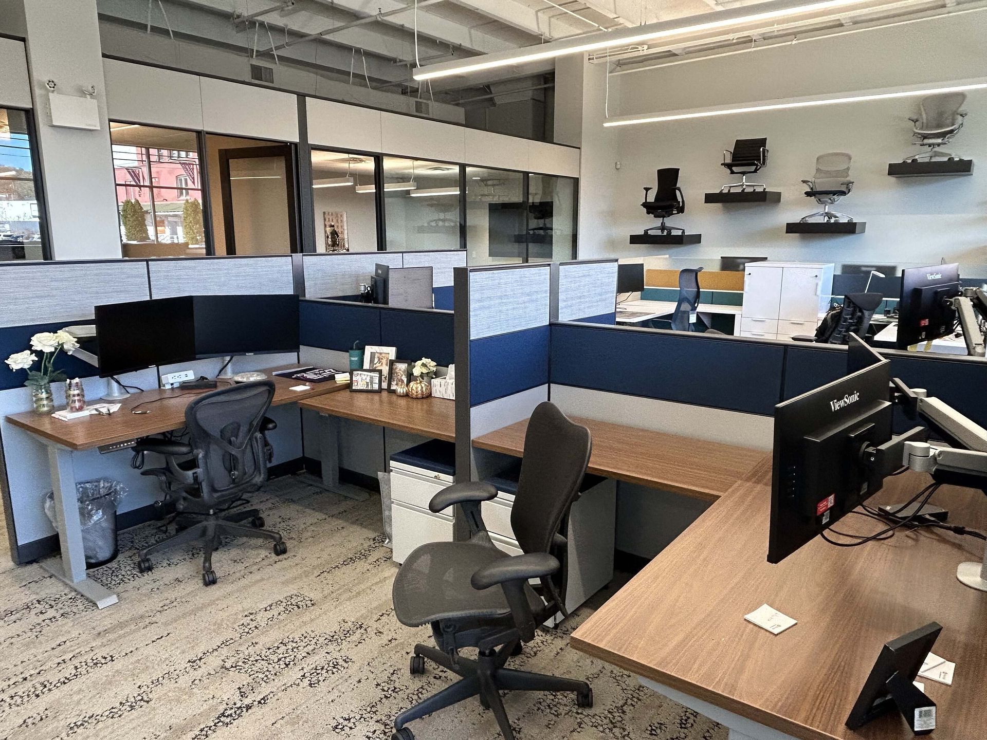 Empty open-plan office with blue cubicle dividers, desks, chairs, and computer monitors