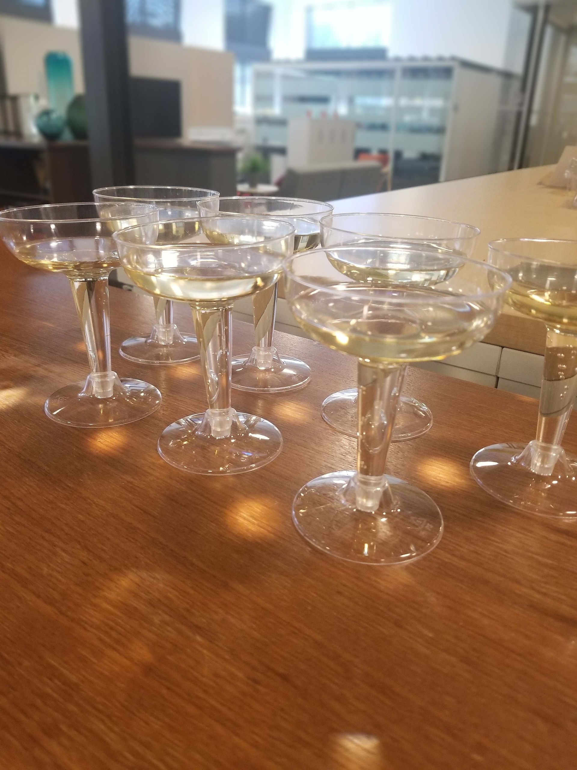 Rows of empty champagne flutes on a wooden table in an office setting